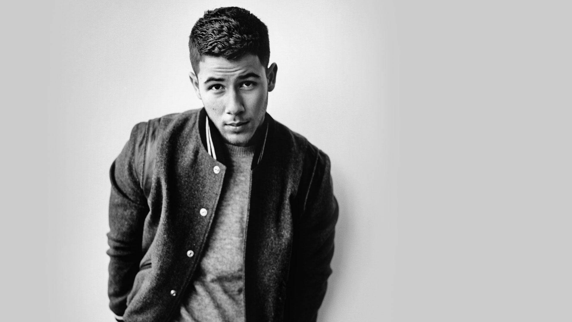 Nick Jonas 桌布 壁紙 — 一名身穿大學外套的年輕男子在純色攝影棚背景前以黑白風格擺出嚴肅表情。