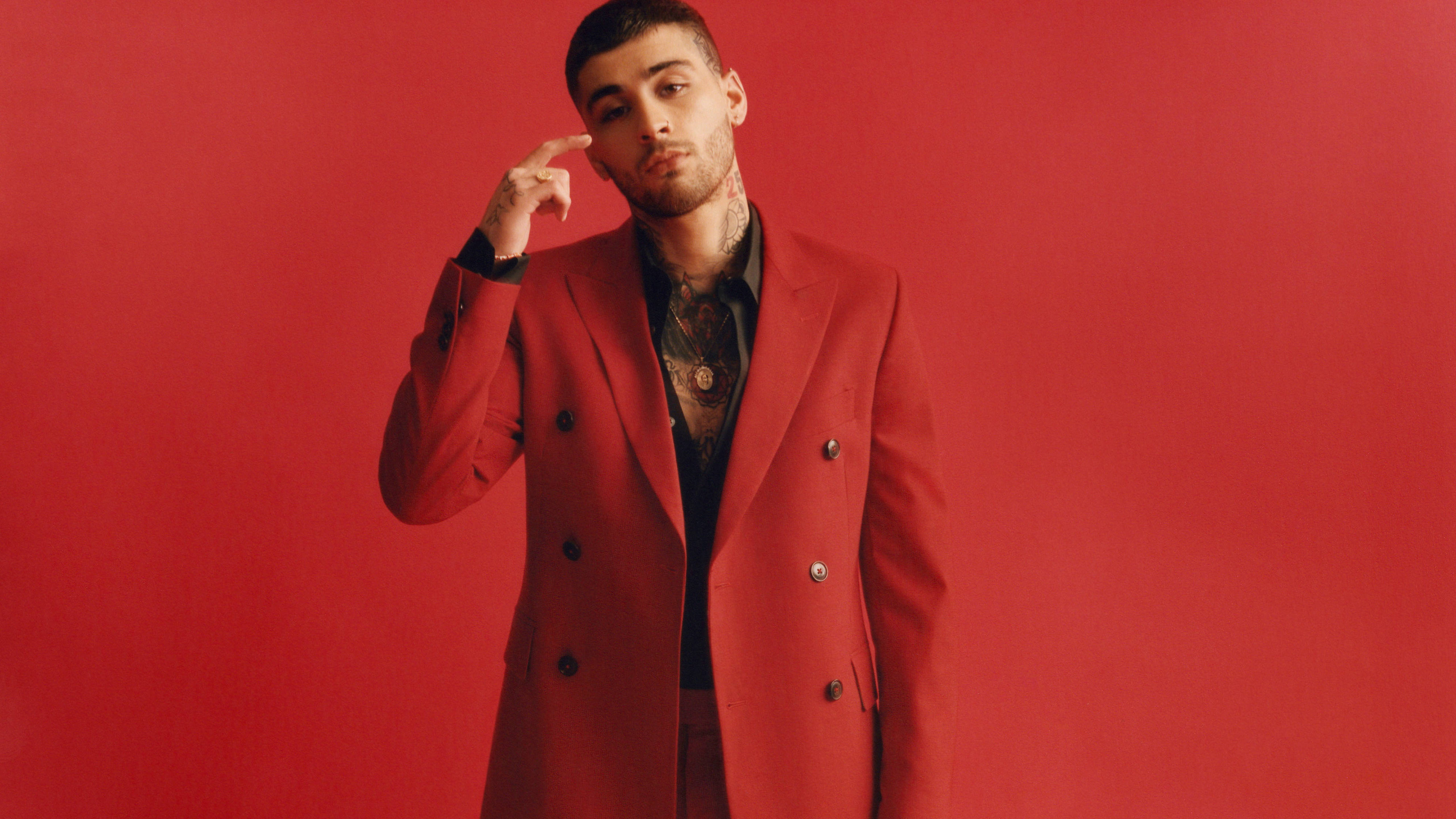 zayn 桌布 壁紙 — 一名身穿大膽紅色雙排扣大衣的男子，手指抵著太陽穴，在純紅色背景前自信地擺姿勢。