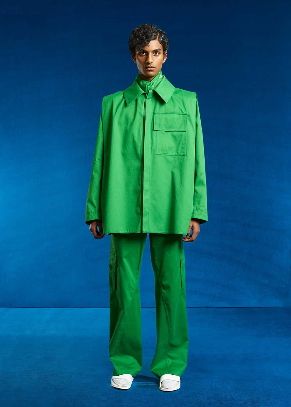 Green Fashion 桌布 壁紙 — 一名身穿大膽綠色服裝的男子，自信地站在深藍色工作室背景前。