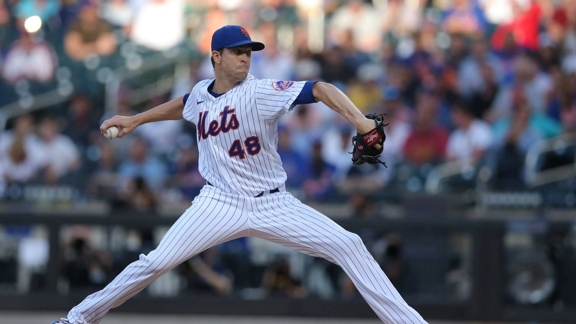 Degrom 桌布 壁紙 — 一名身穿大都會隊球衣的棒球投手在陽光明媚的球場上投球，背景是模糊的人群。