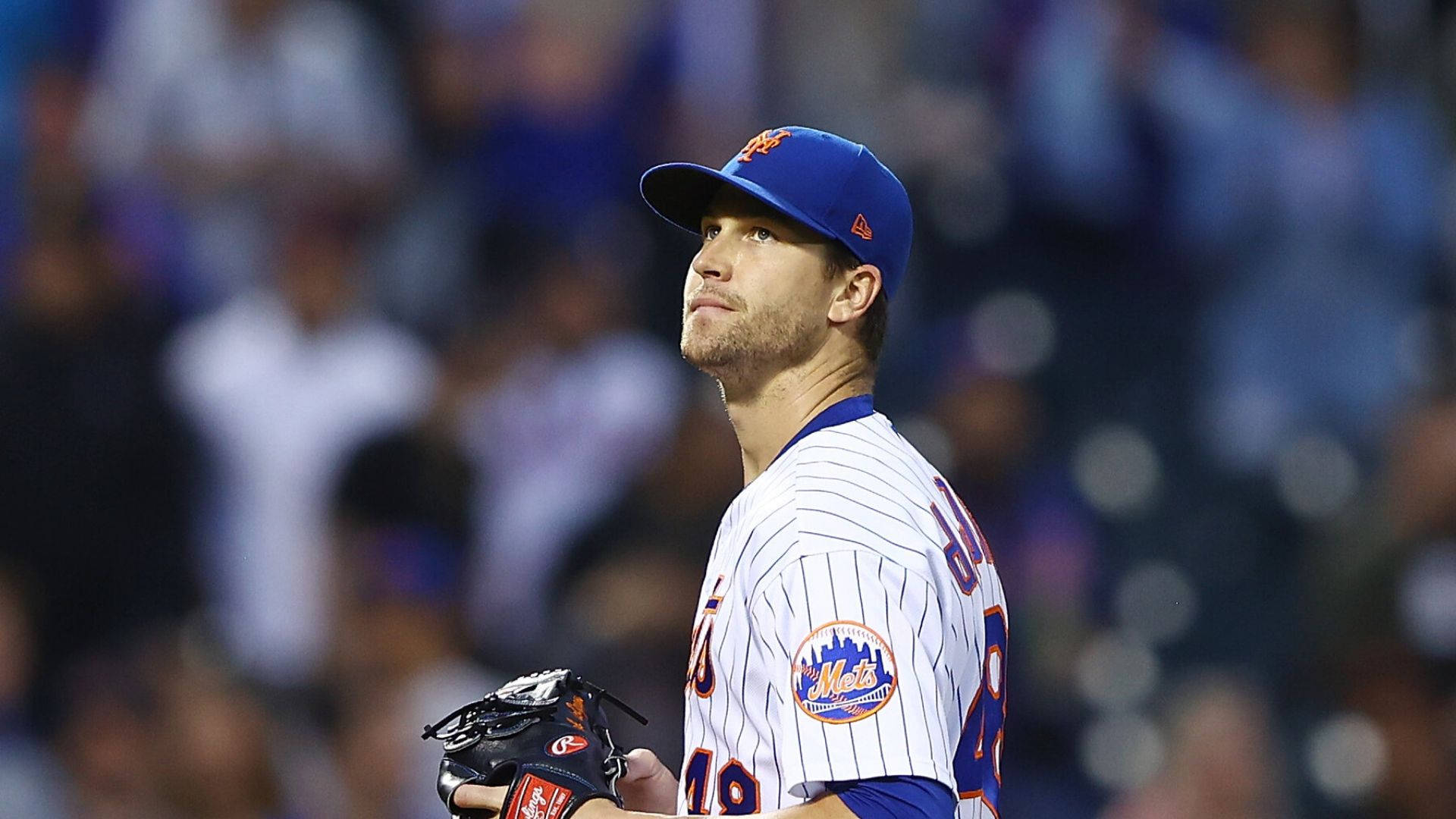Degrom 桌布 壁紙 — 一名身穿大都會隊球衣的棒球投手在球場燈光下專注地站在場上，背景是模糊的球迷。