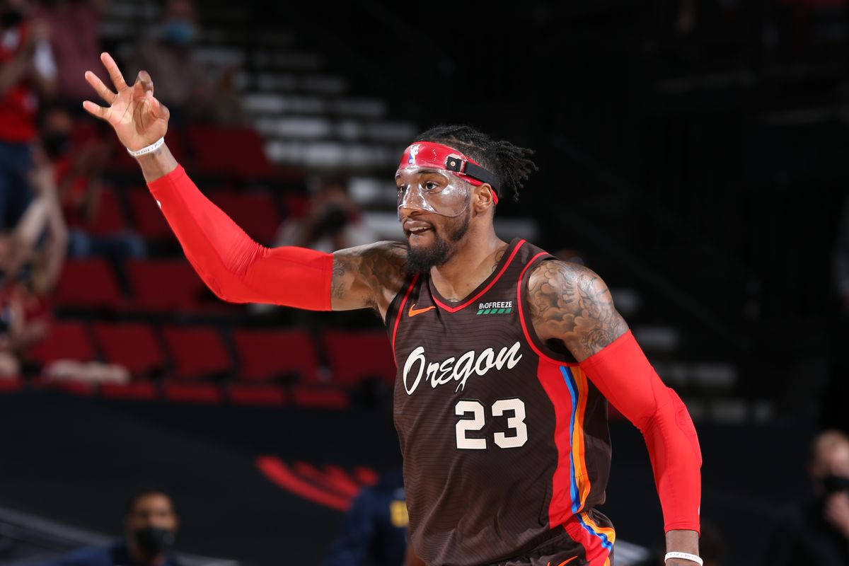 robert covington 桌布 壁紙 — 一名身穿奧勒岡州球衣的籃球運動員在燈光昏暗、設有紅色座位的場館內向球迷揮手。
