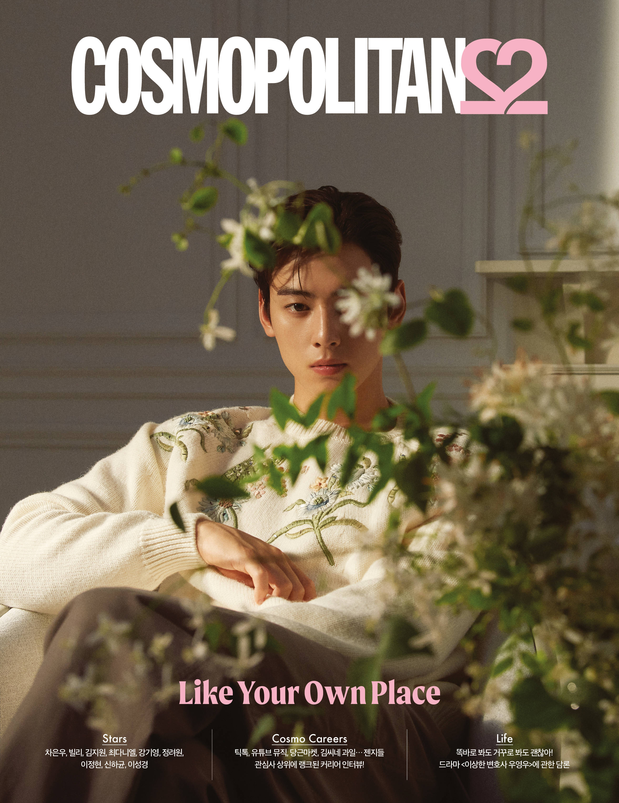 Eunwoo 桌布 壁紙 — 一名身穿奶油色毛衣的男子靜靜地坐著，白色花朵和綠色植物在柔和的灰色牆壁襯托下框住他的臉龐。