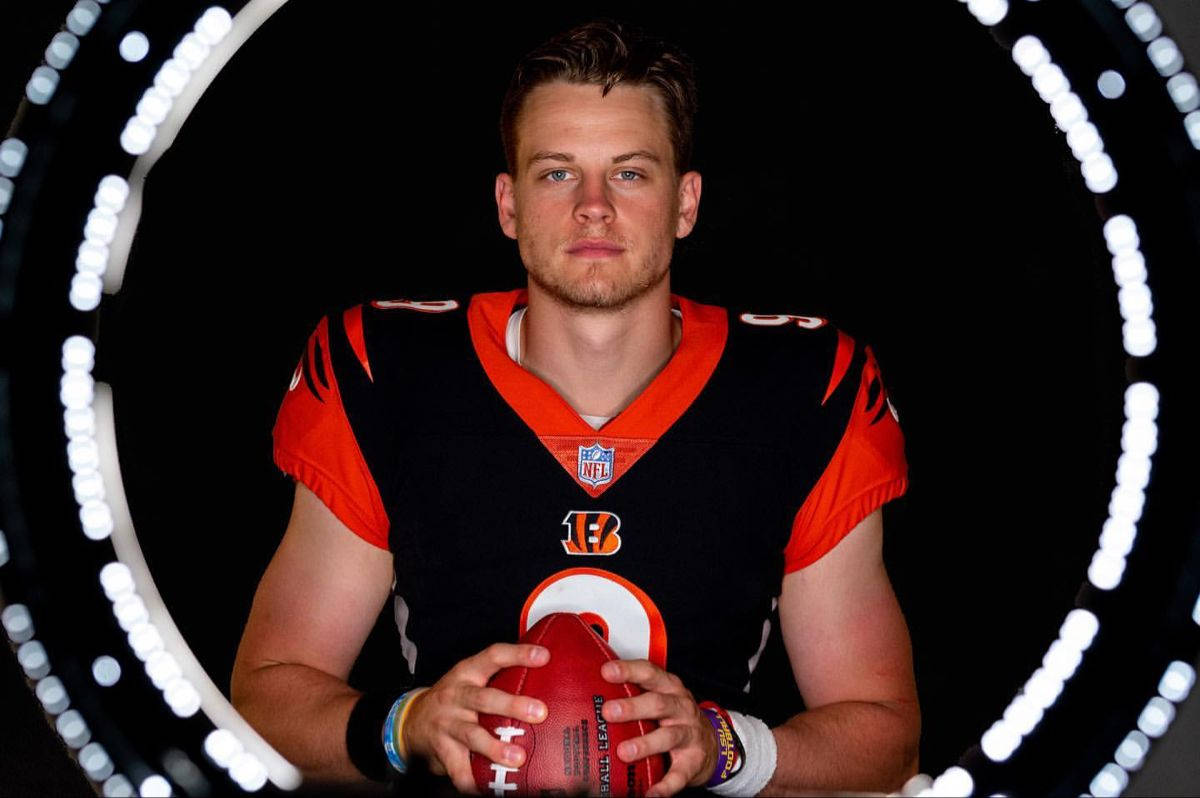 Joe Burrow 桌布 壁紙 — 一名身穿孟加拉虎隊球衣的美式足球四分衛，在黑色背景上，手持一個被發光圓形光環框住的球。