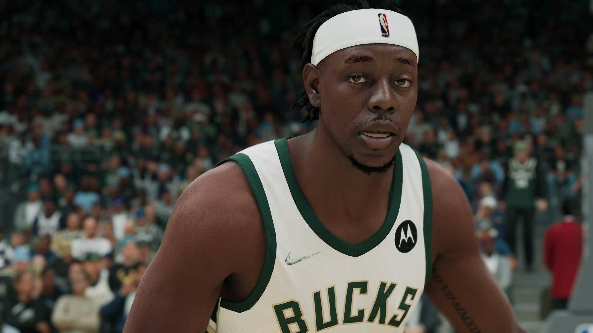 Jrue Holiday 桌布 壁紙 — 一名身穿密爾瓦基公鹿隊球衣的籃球運動員在比賽中專注地凝視，身後是座無虛席的球場。