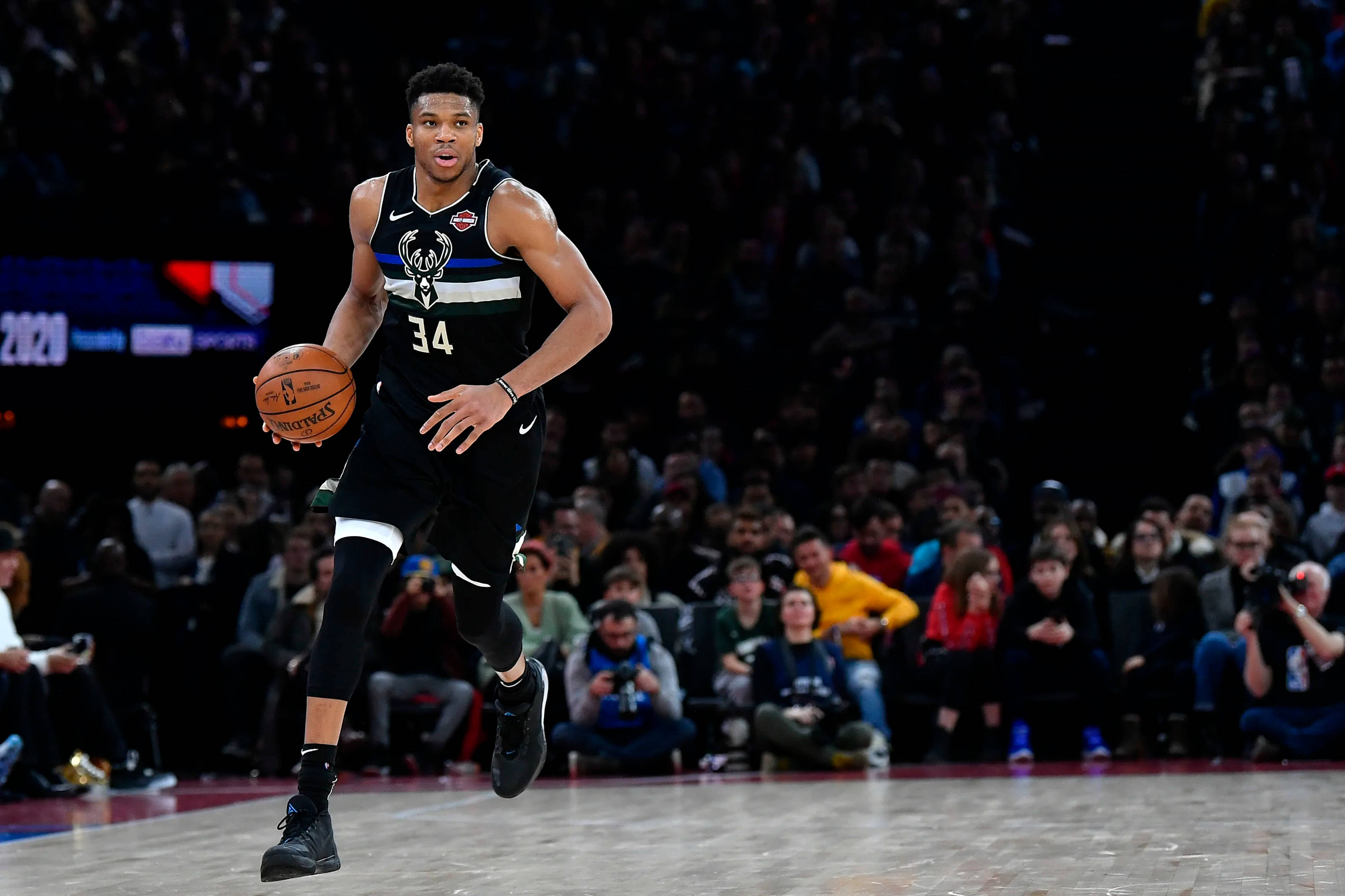Giannis 桌布 壁紙 — 一名身穿密爾瓦基公鹿隊球衣的籃球運動員在明亮的場館燈光下，在比賽中運球前進。