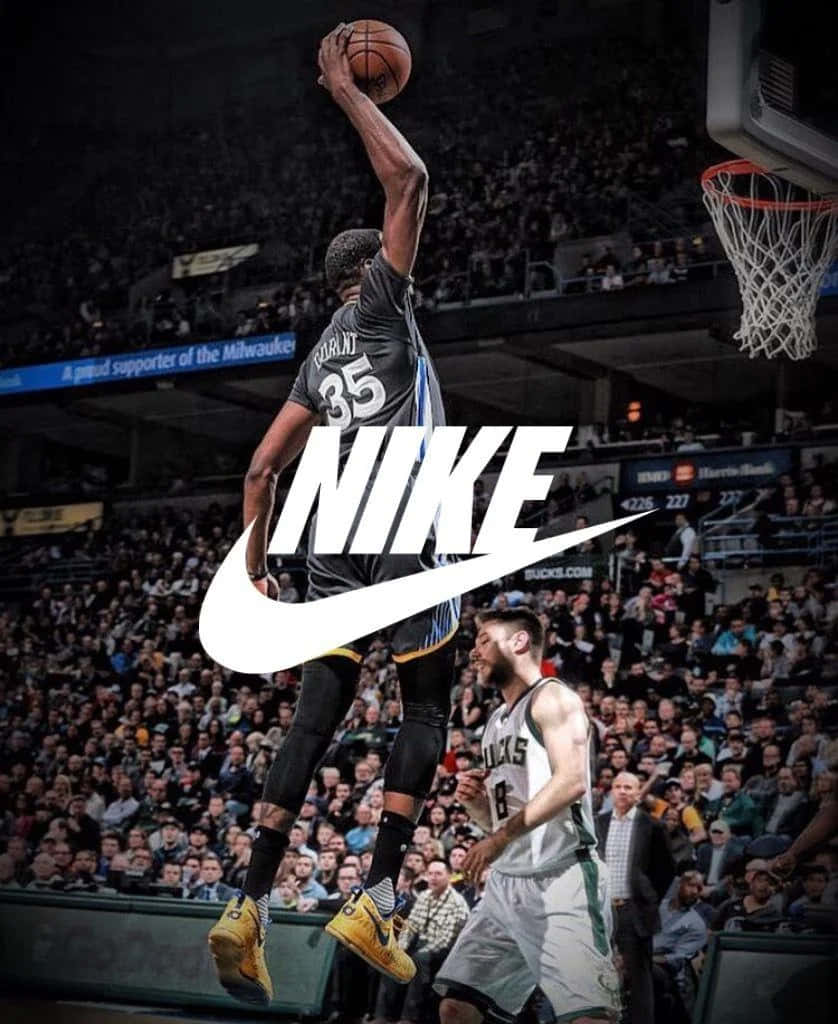 Nike 節奏籃球 桌布 壁紙 — 一名身穿密爾瓦基公鹿隊球衣的籃球運動員飛身灌籃，防守球員在下方觀看，場館內座無虛席。
