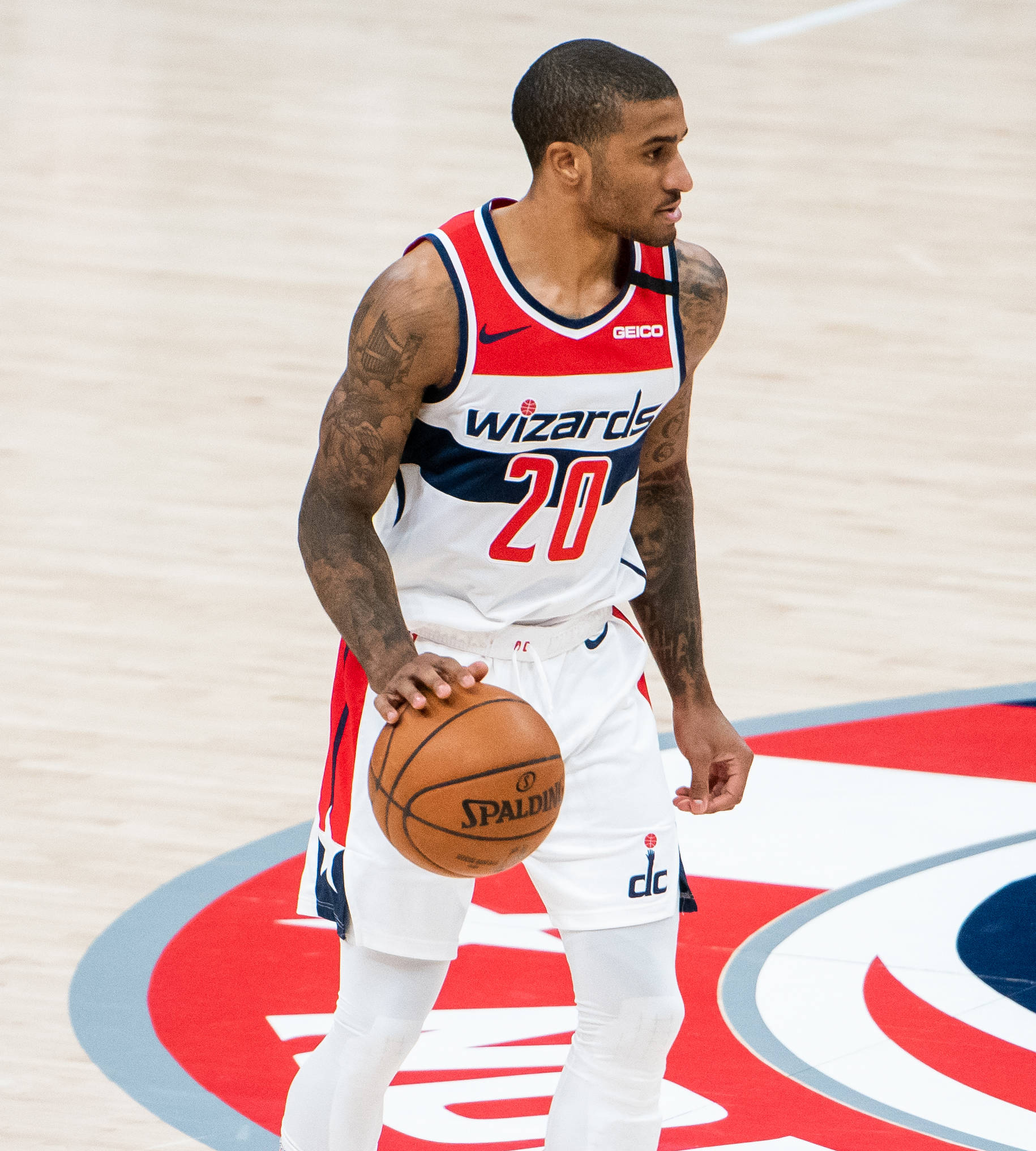NBA 桌布 壁紙 — 一名身穿巫師隊球衣的籃球運動員，在明亮的場館燈光下，於帶有球隊標誌的球場上手持 Spalding 籃球。