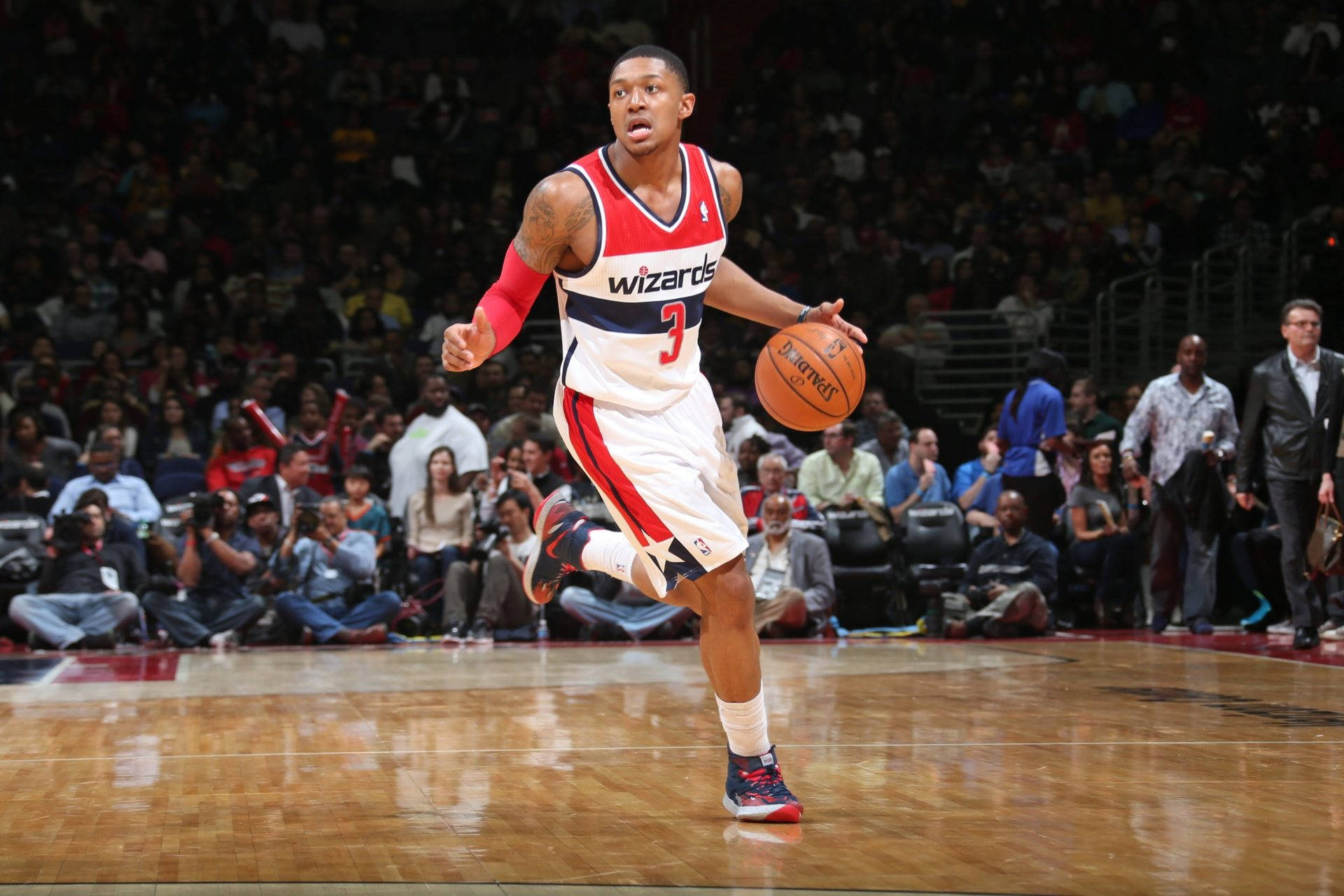 Bradley Beal 桌布 壁紙 — 一名身穿巫師隊球衣的籃球運動員在比賽中運球，背景是座無虛席的球場。