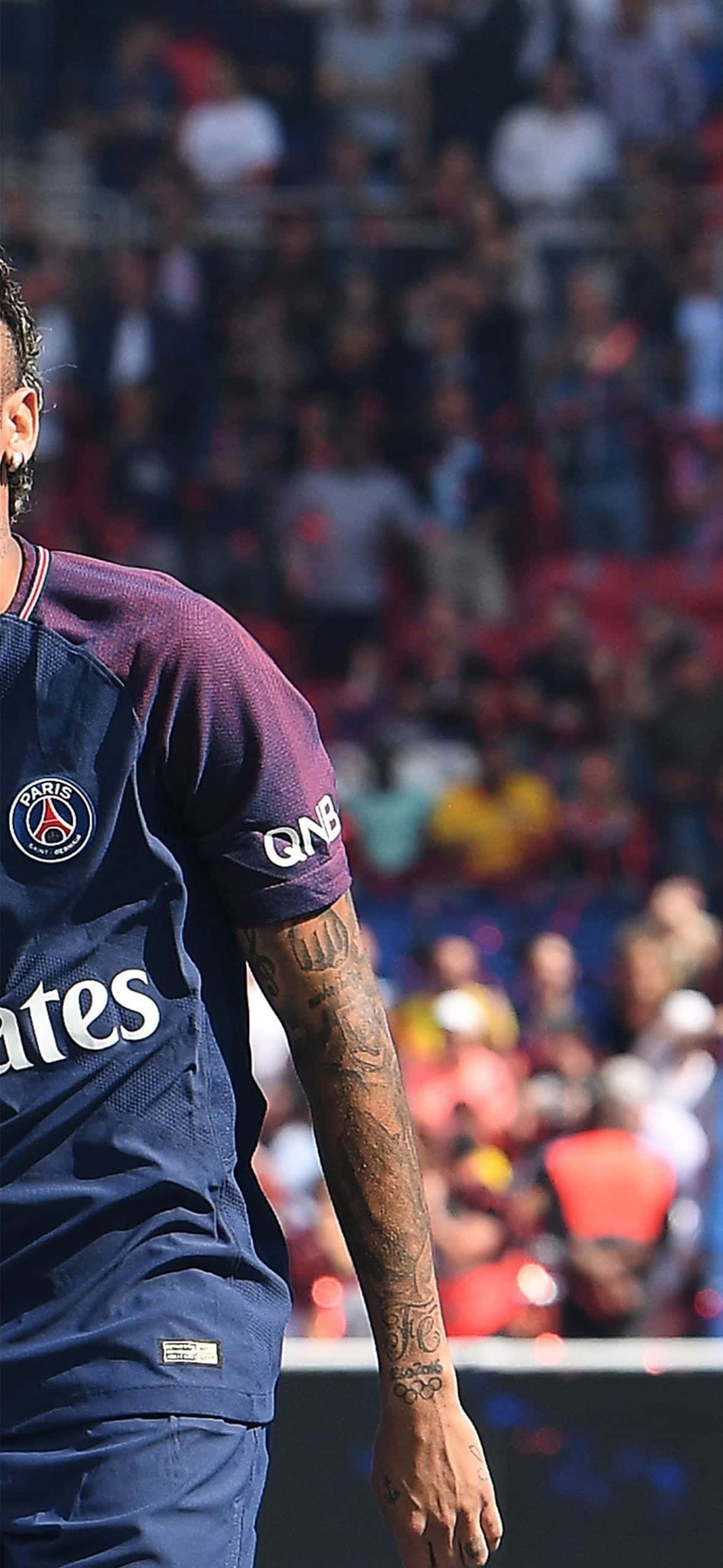Neymar iPhone 桌布 壁紙 — 一名身穿巴黎聖日耳曼球衣的足球員站在球場上，背景是模糊的球迷。