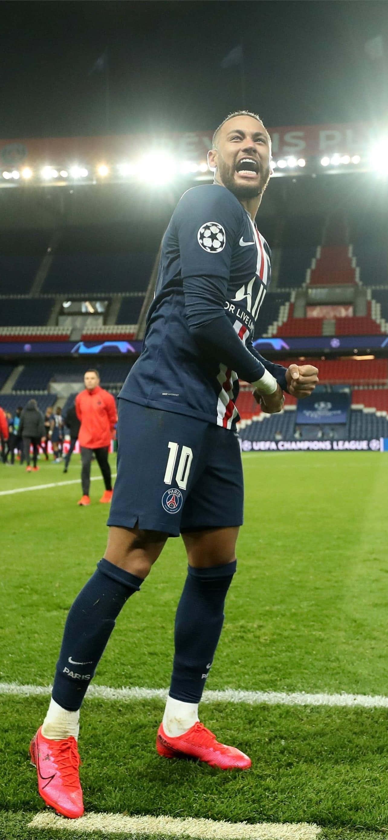 Neymar iPhone 桌布 壁紙 — 一名身穿巴黎聖日耳曼球衣的足球運動員在夜間燈光明亮的球場上熱情慶祝。