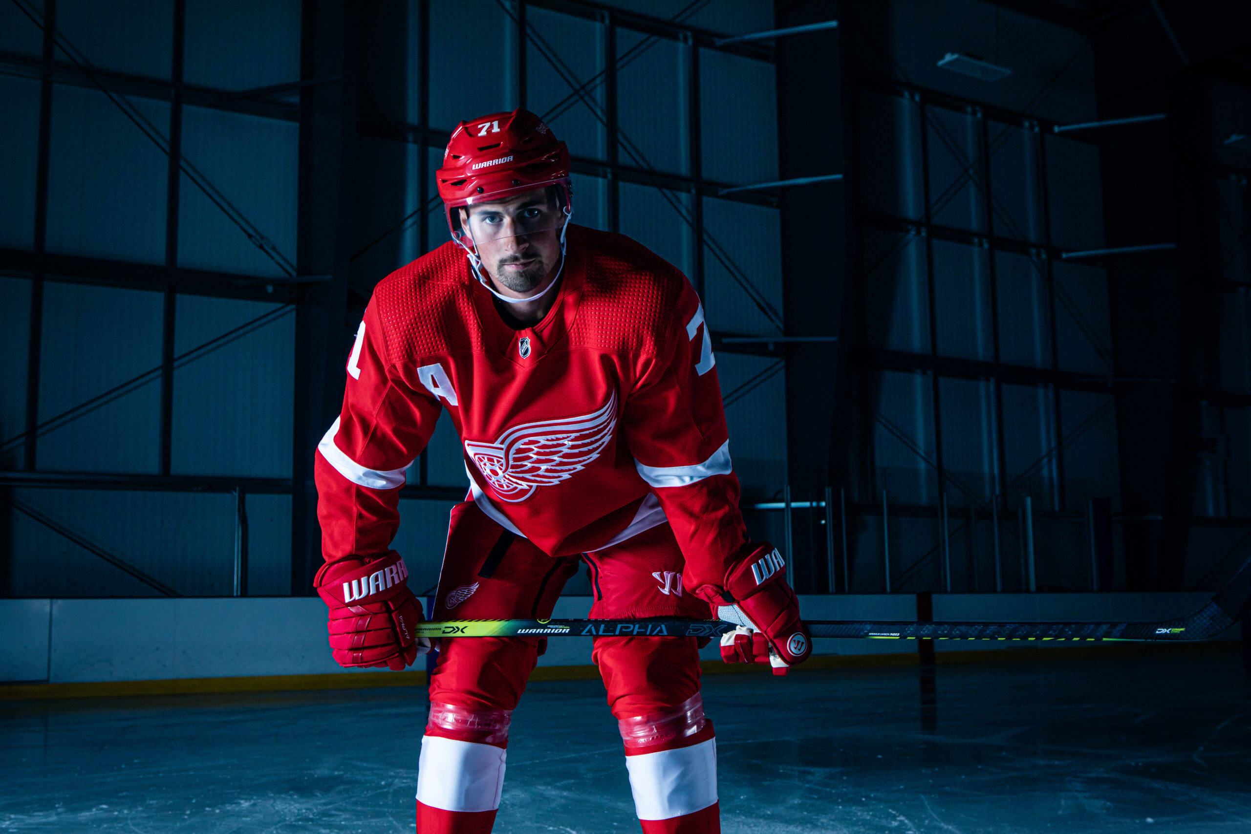 hockey 桌布 壁紙 — 一名身穿底特律紅翼紅色裝備的冰球運動員，在戲劇性的藍色燈光下，在冰上保持高度專注。