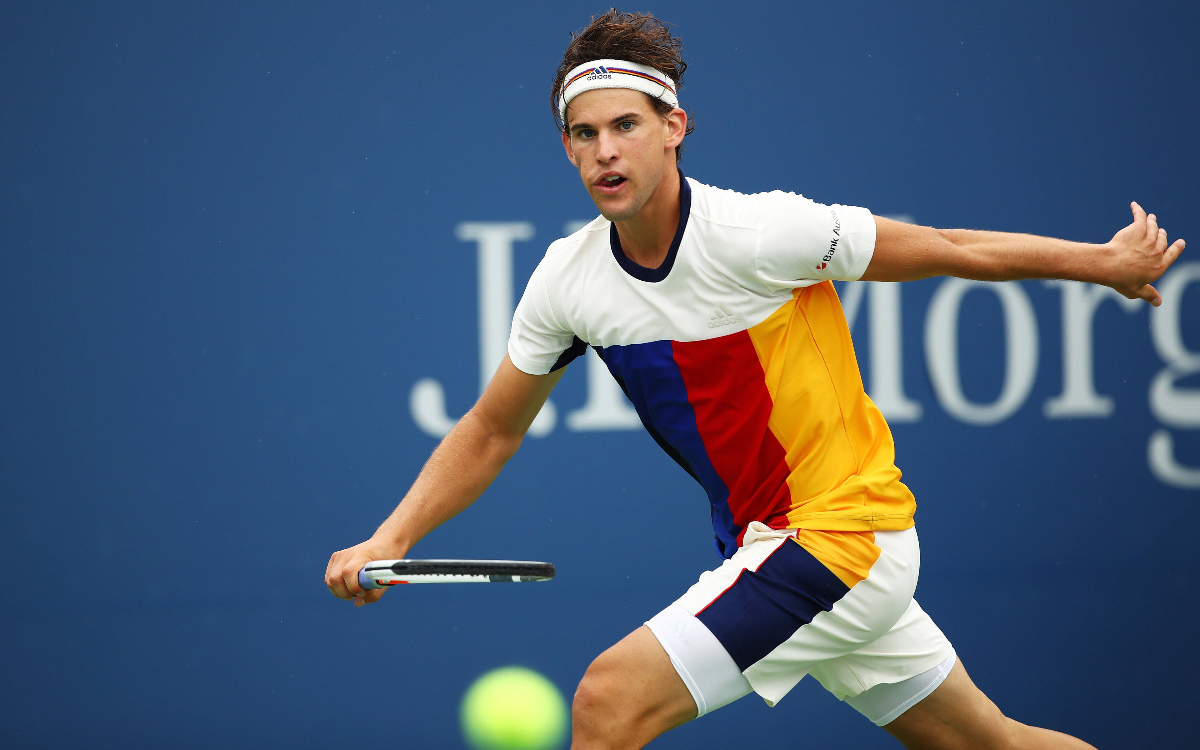 dominic thiem 桌布 壁紙 — 一名身穿彩色襯衫的男性網球選手向前衝刺，擊打一顆亮黃色的網球，對著一面純藍色的牆壁。