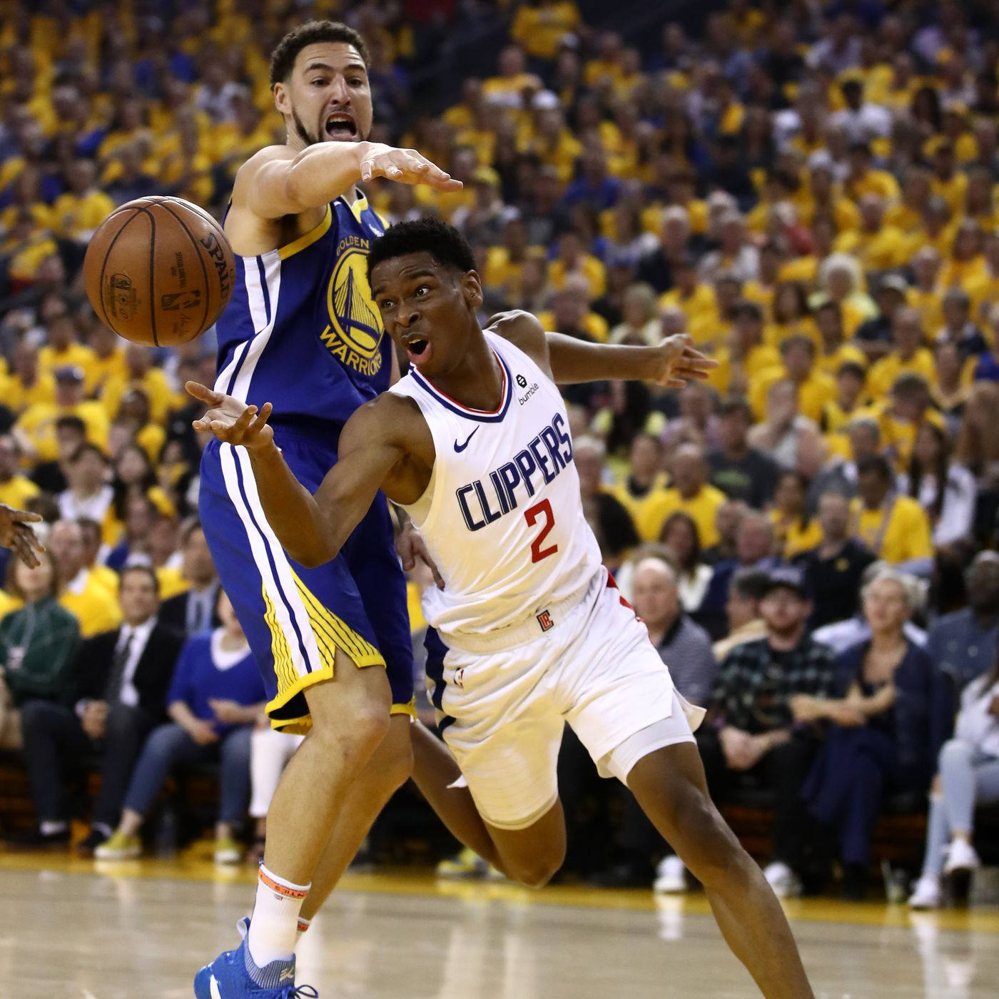 NBA 桌布 壁紙 — 一名身穿快艇隊球衣的籃球運動員在擠滿人的黃色體育館中運球，同時被勇士隊球員緊密防守。