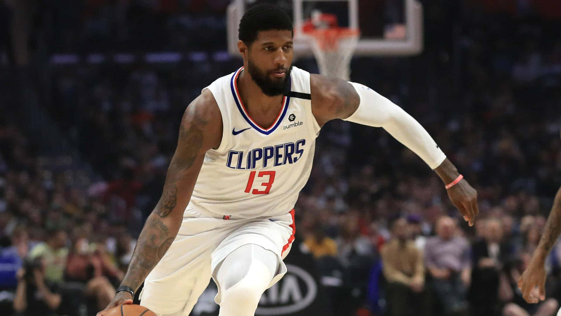 Paul George Clippers 桌布 壁紙 — 一名身穿快艇隊球衣的籃球運動員在明亮的場館燈光下，專注地運球，進行一場激烈的比賽。