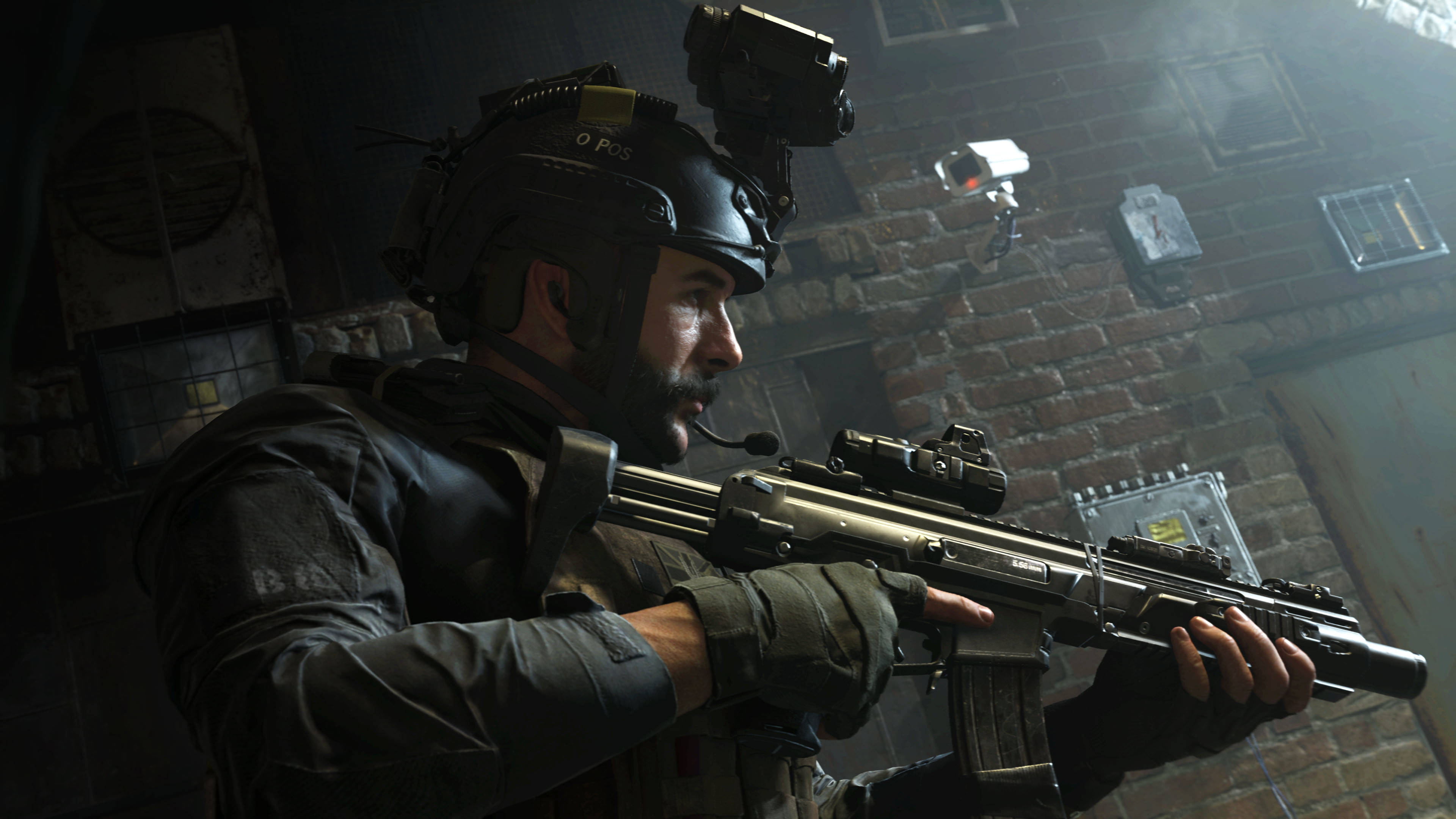 4K call of duty 桌布 壁紙 — 一名身穿戰術裝備的士兵在昏暗的磚牆城市環境中，在監控攝影機下瞄準步槍。