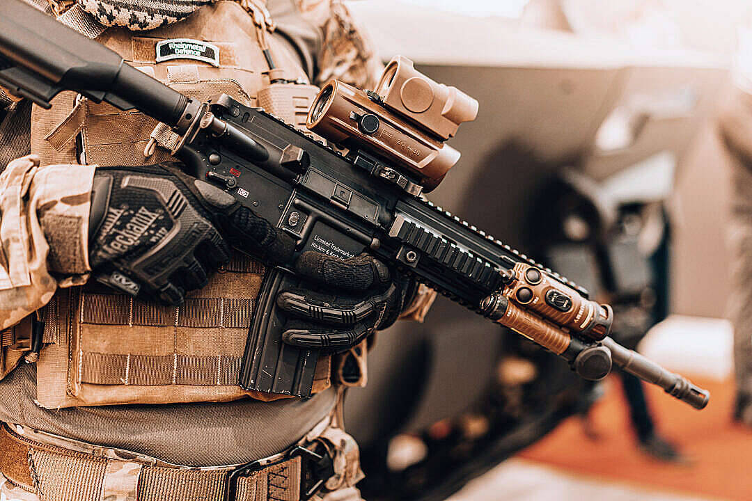 Shooting 桌布 壁紙 — 一名身穿戰術裝備的士兵手持配備光學瞄準器和配件的現代突擊步槍的特寫。