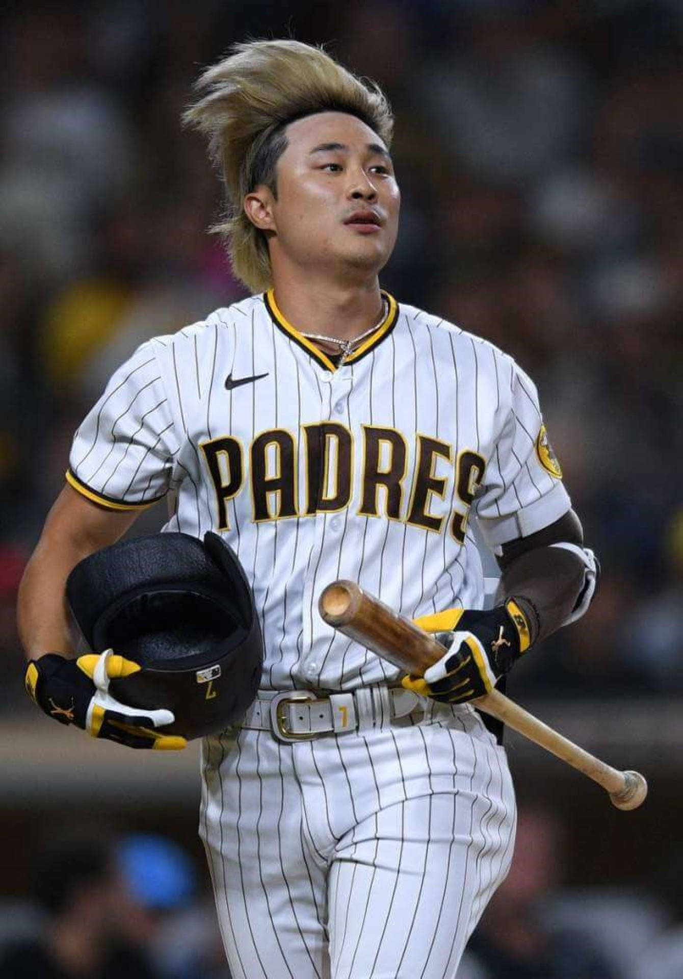 Padres 桌布 壁紙 — 一名身穿教士隊球衣的棒球運動員，在球場燈光下揮舞球棒，頭盔下的頭髮飛揚。