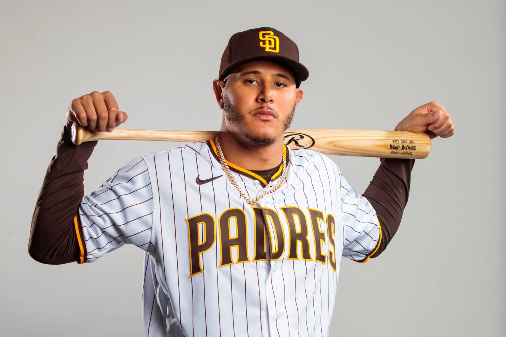 Padres 桌布 壁紙 — 一名身穿教士隊球衣的棒球運動員，在純灰色背景前將球棒扛在肩上。