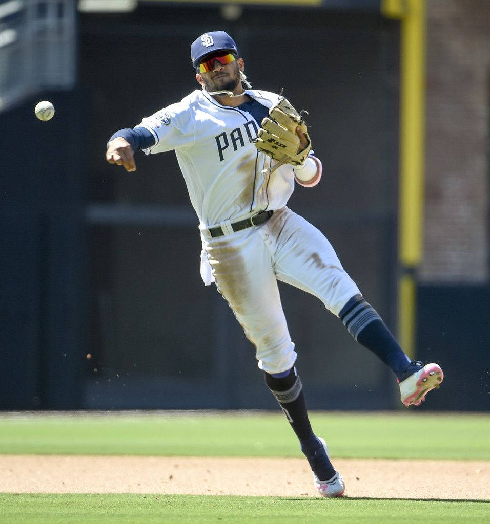 Tatis 桌布 壁紙 — 一名身穿教士隊球衣的棒球選手在陽光明媚的球場上以動態動作將球擲向空中。