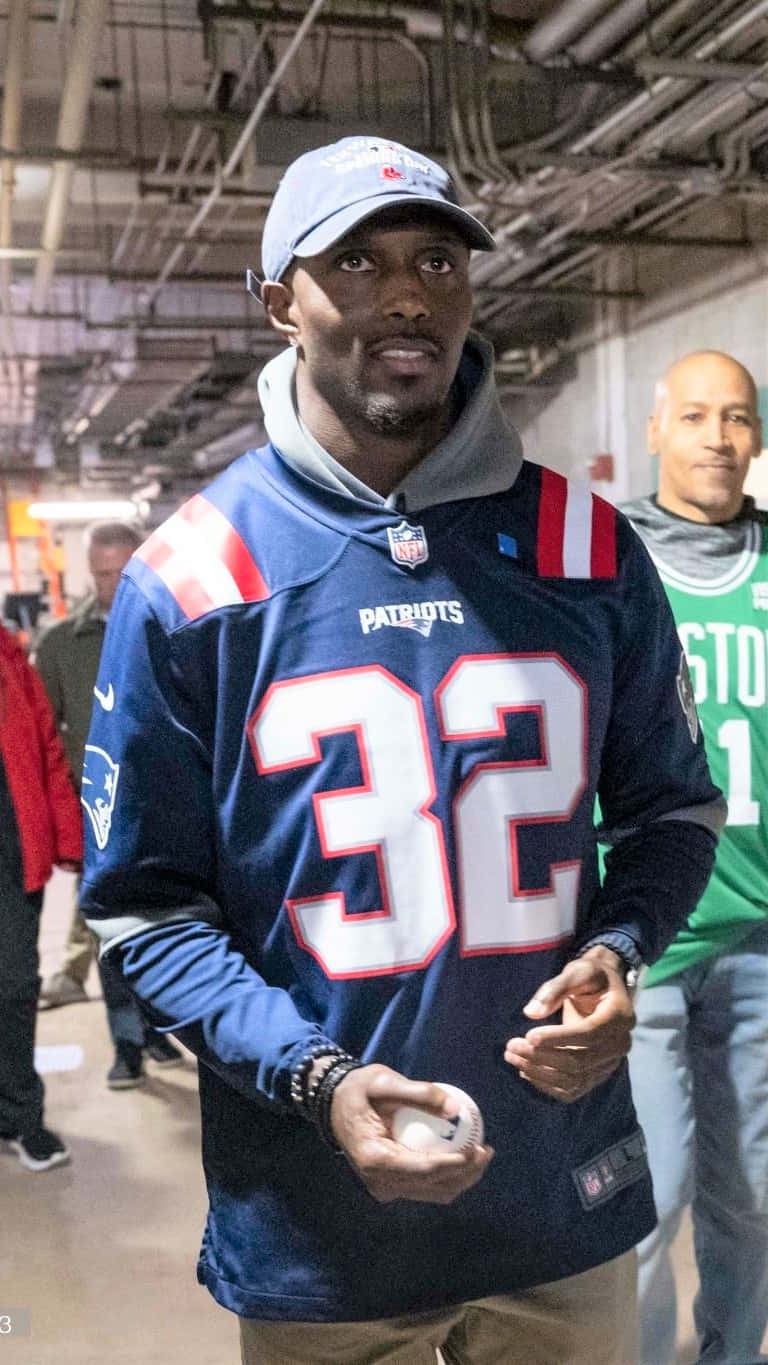 Devin Mccourty 桌布 壁紙 — 一名身穿新英格蘭愛國者隊32號球衣的男子在室內人造燈光下手持棒球。