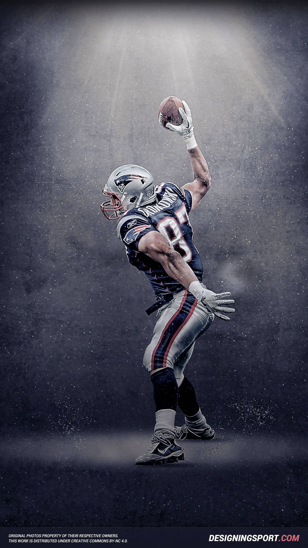 Patriots 桌布 壁紙 — 一名身穿新英格蘭愛國者隊球衣的足球運動員在黑暗迷霧背景下，戲劇性地跳起接住一個足球，聚光燈光束照射。