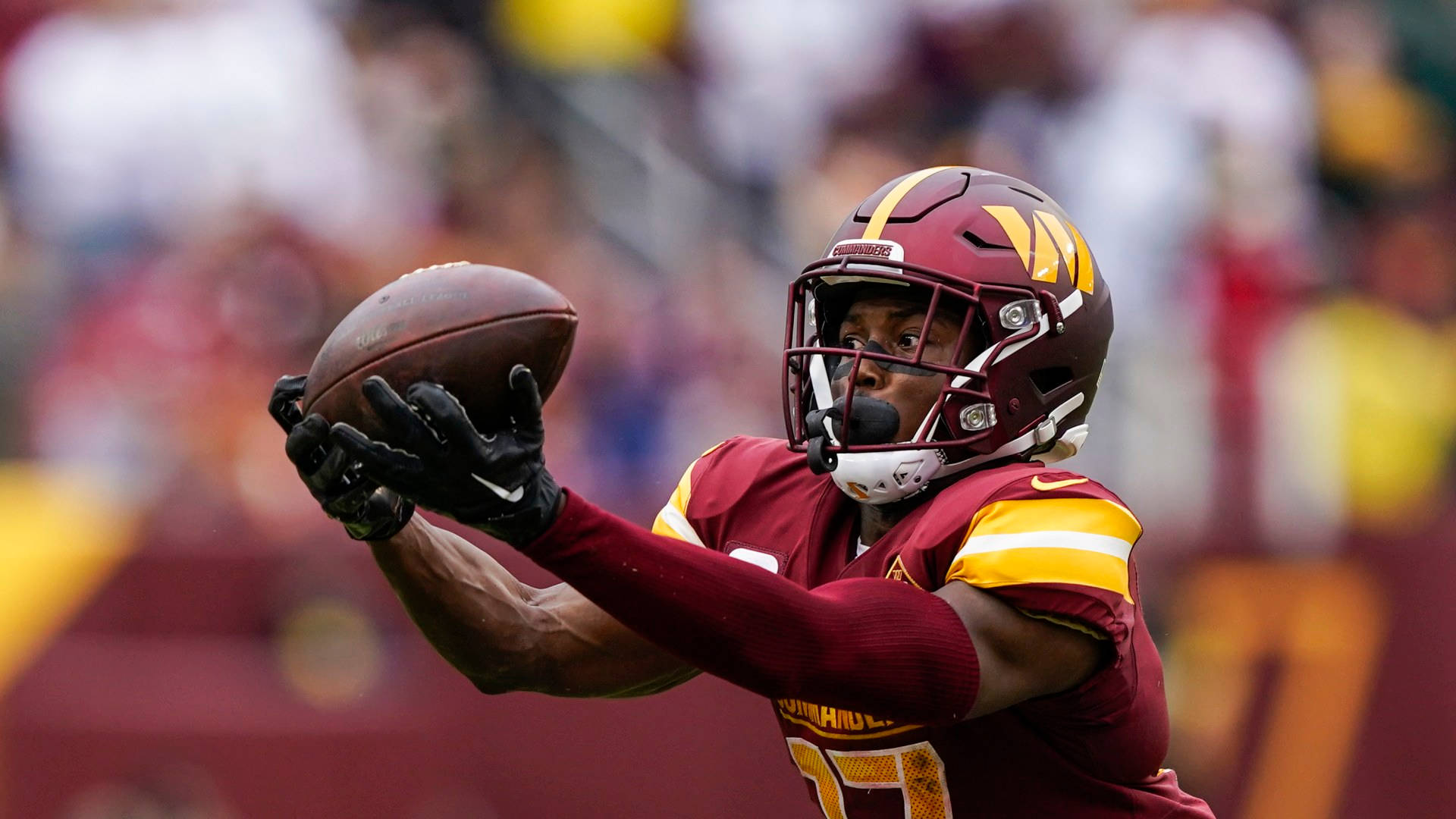 Football Players 桌布 壁紙 — 一名身穿栗色和金色球衣的足球員在比賽中專注地接住球。