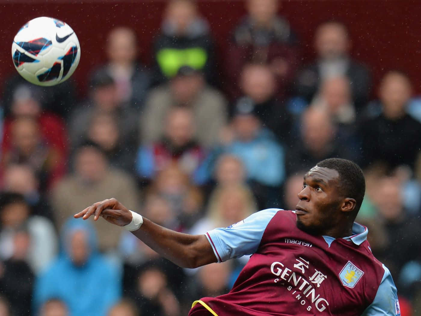 Aston Villa Fc 桌布 壁紙 — 一名身穿栗色球衣的足球運動員在雨中比賽中凌空頭球，背景是模糊的觀眾。