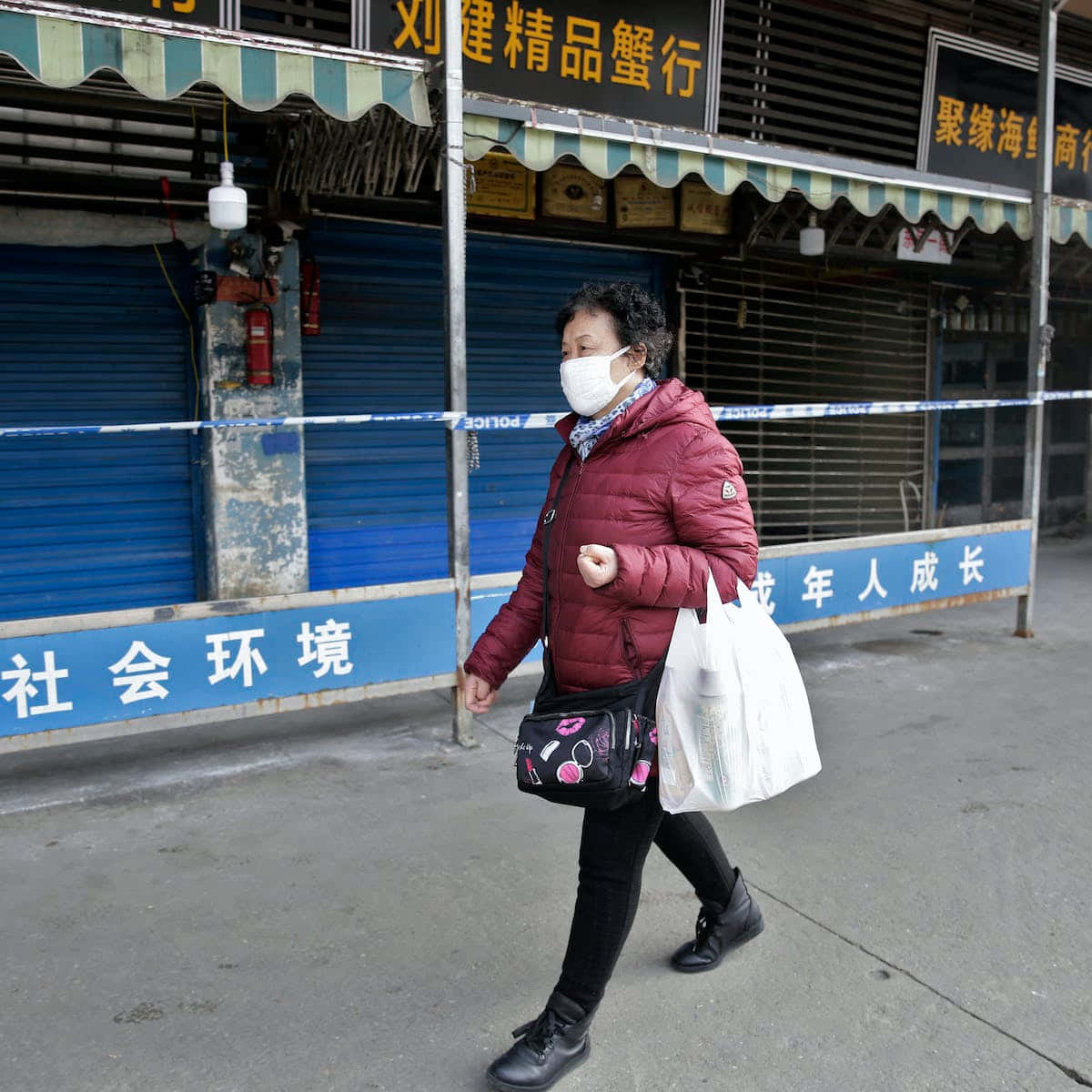 中國 桌布 壁紙 — 一名身穿栗色羽絨外套和口罩的女子走過被警方封條封鎖的關閉店舖。