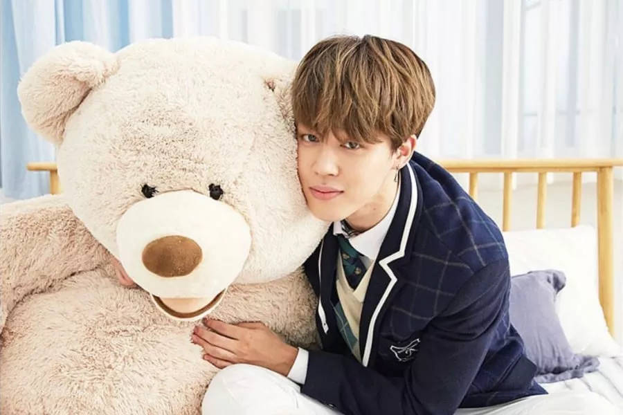 Bts Jimin 桌布 壁紙 — 一名身穿校服的年輕男子在床上深情地靠著一隻巨大的毛絨泰迪熊。