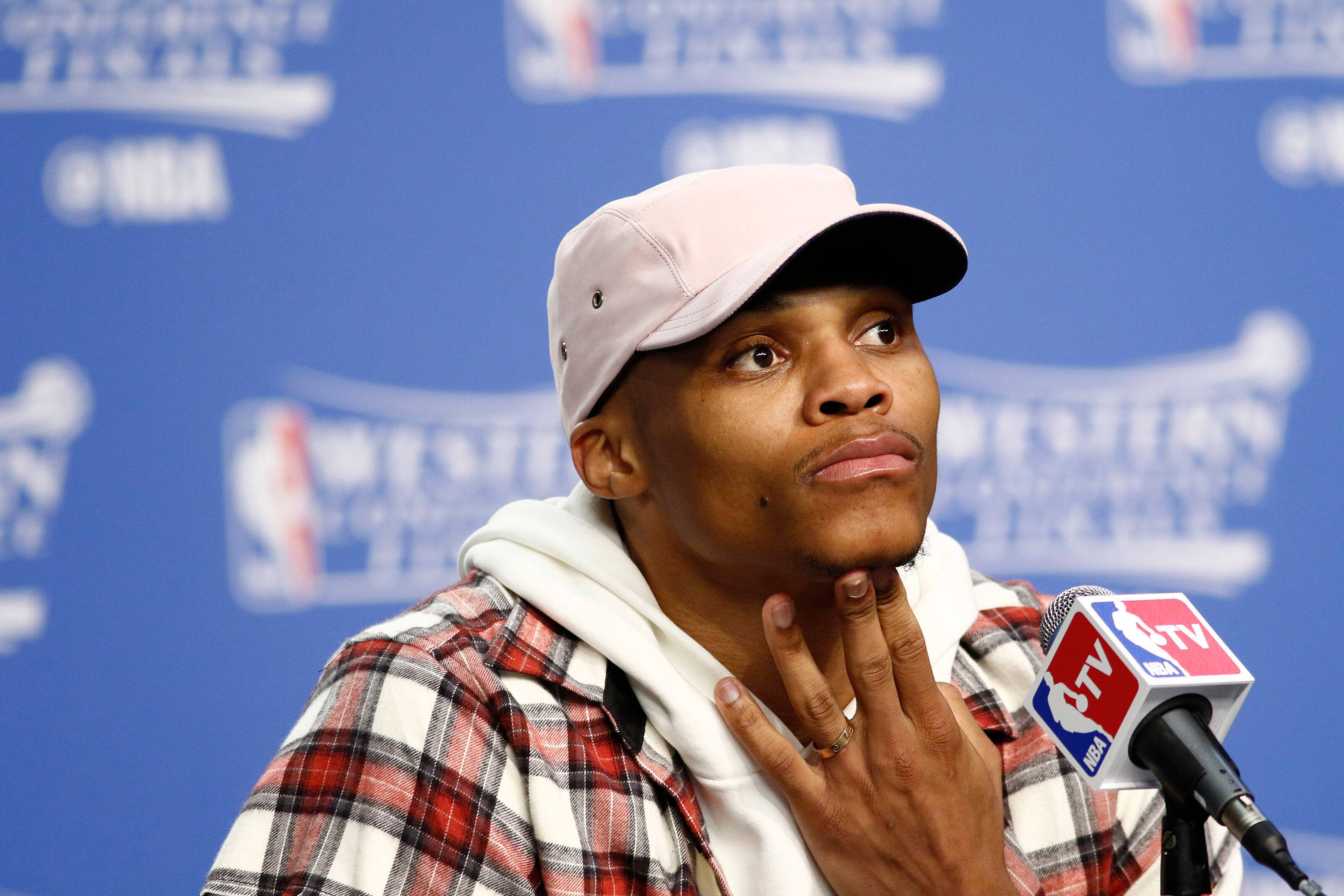 Westbrook 桌布 壁紙 — 一名身穿格紋襯衫和帽子的籃球運動員在記者會上對著NBA TV麥克風說話，若有所思地向上凝視。