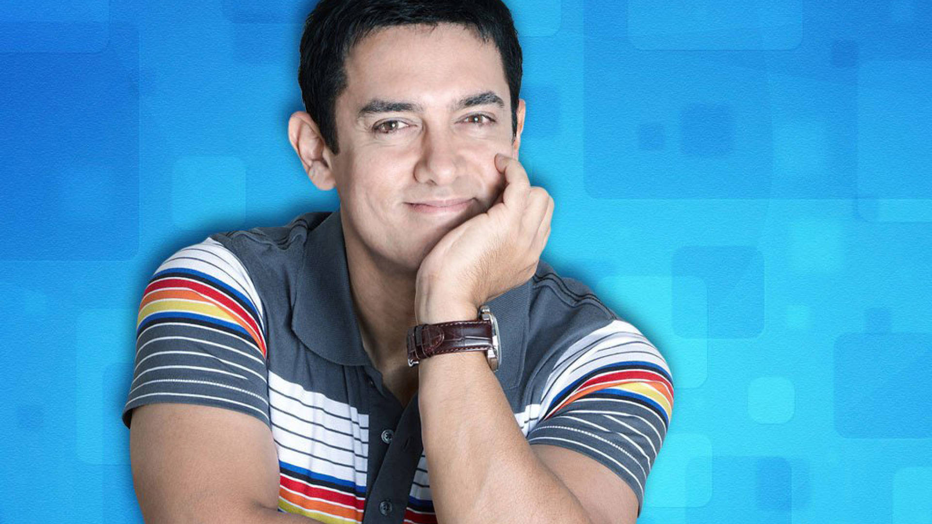 Aamir Khan 桌布 壁紙 — 一名身穿條紋Polo衫的男子，在藍色幾何背景前用手托著下巴。