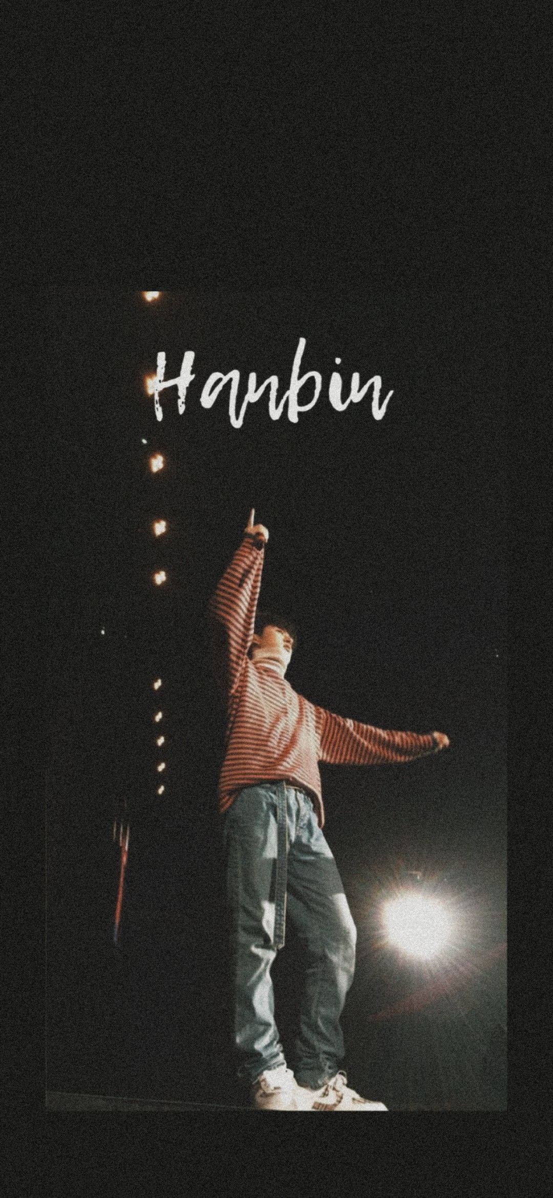 kim hanbin 桌布 壁紙 — 一名身穿條紋襯衫的人站在舞台上，明亮的聚光燈下，上方寫著Hanbin的名字。