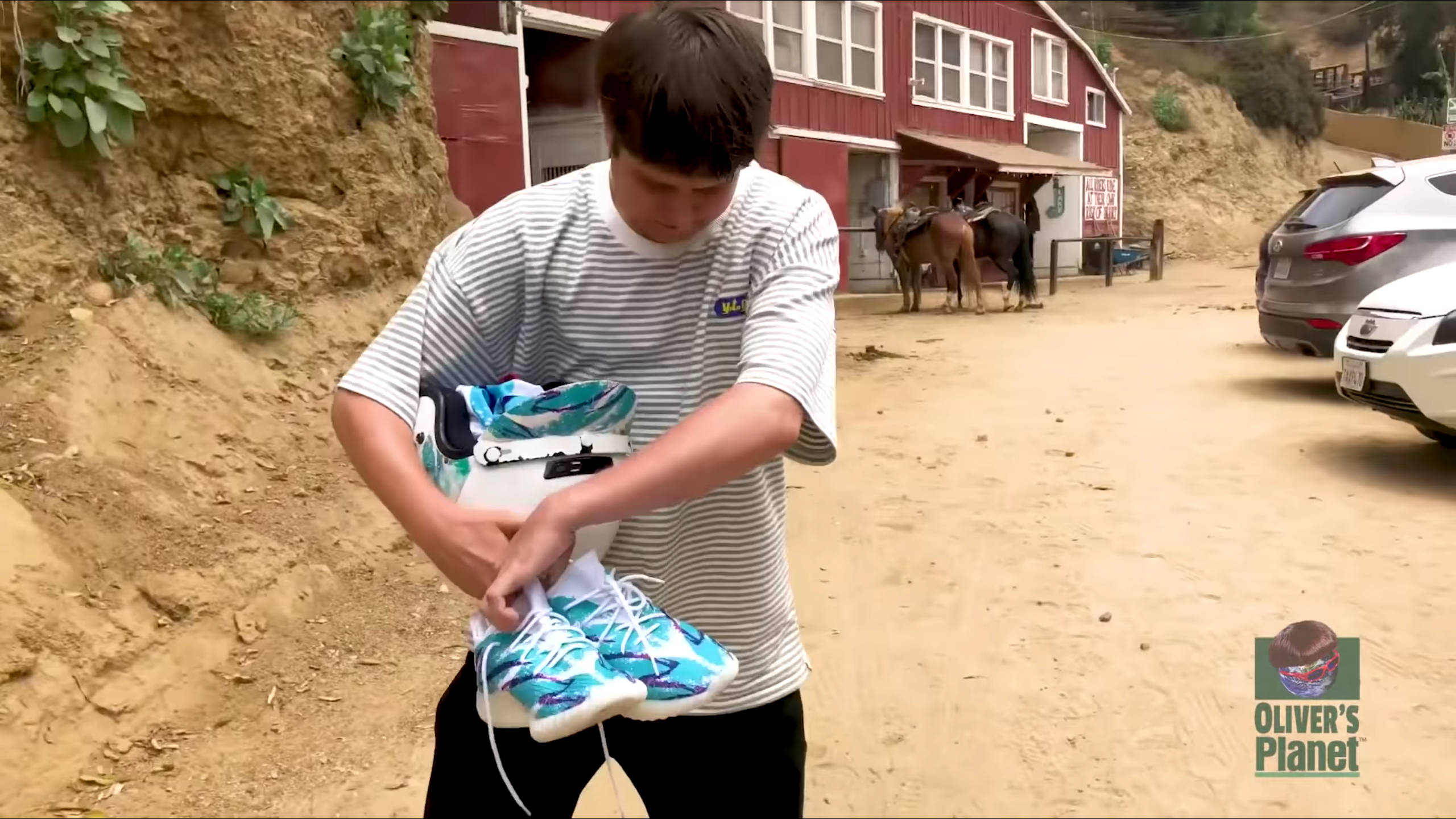 oliver 桌布 壁紙 — 一名身穿條紋襯衫的年輕男子在塵土飛揚的鄉村道路上，靠近一個有馬匹的紅色穀倉，繫著鮮豔藍白運動鞋的鞋帶。