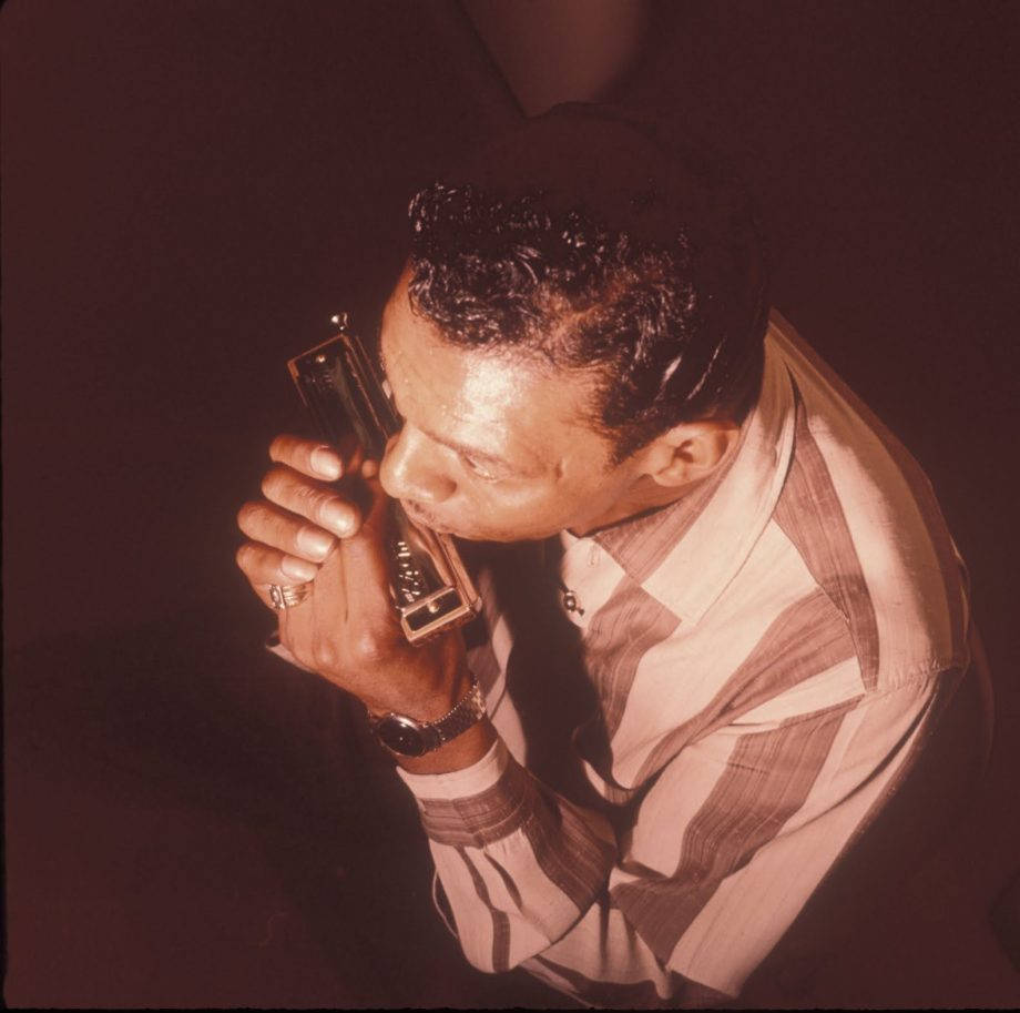 Little Walter 桌布 壁紙 — 一名身穿條紋襯衫的男子在黑暗背景下，於溫暖的聚光燈下熱情地吹奏口琴。