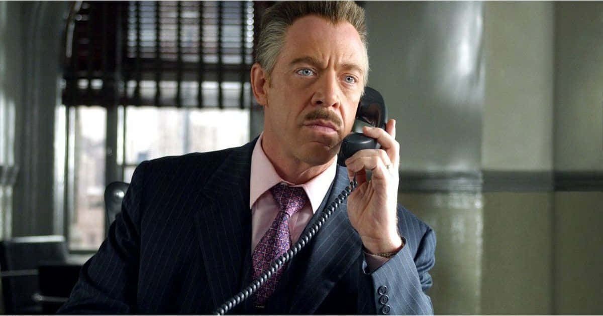 J Jonah Jameson 桌布 壁紙 — 一名身穿條紋西裝的男子在現代辦公室裡，表情嚴肅地將電話貼在耳邊。