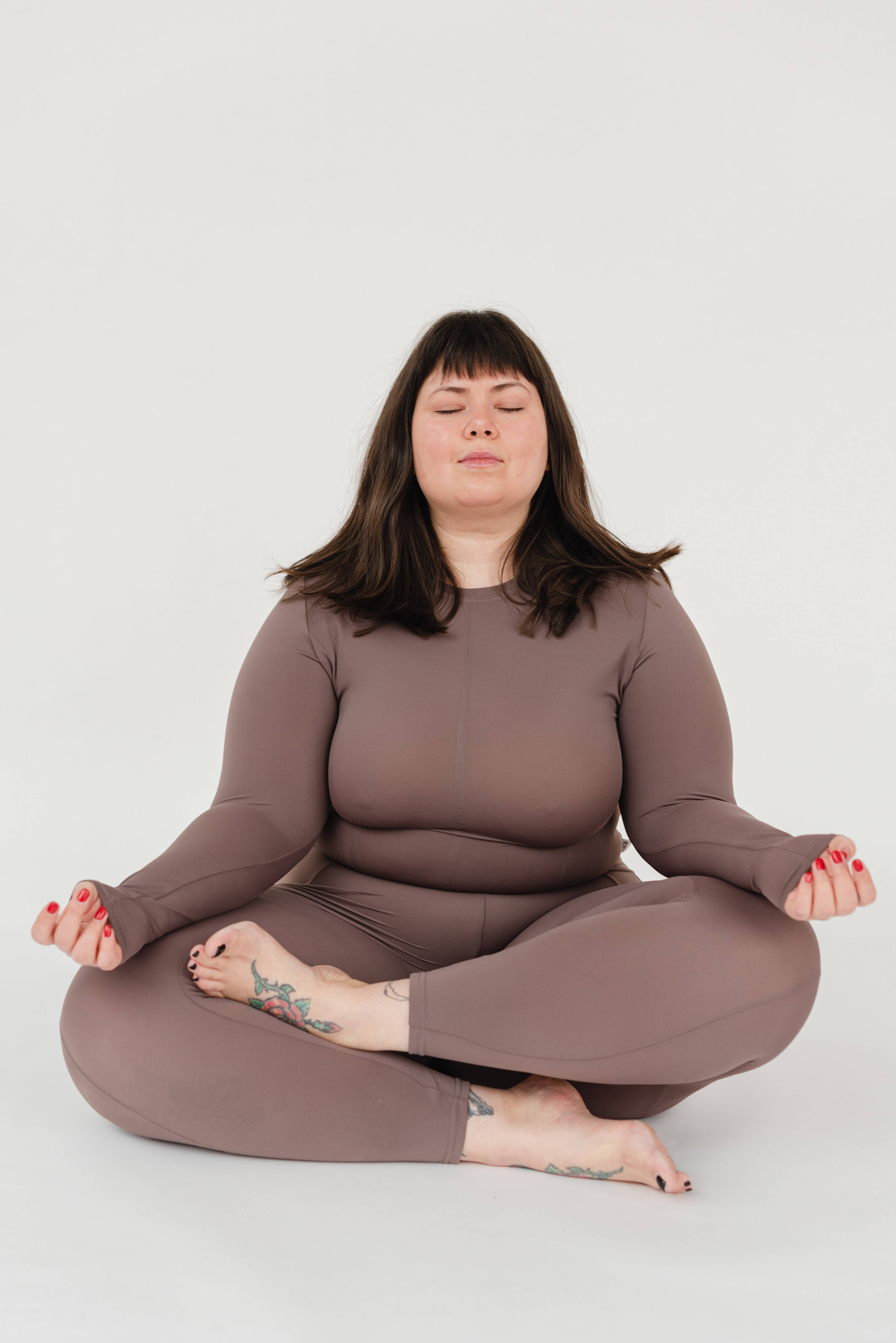 Meditation 桌布 壁紙 — 一名身穿棕色休閒服的女性在純白色背景前閉眼盤腿冥想。