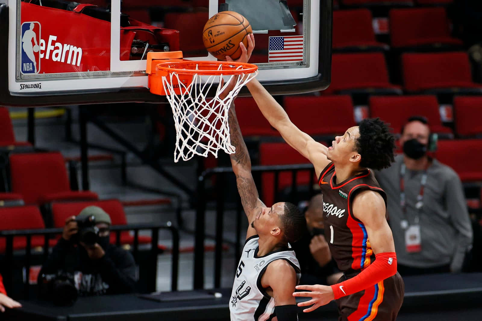 NBA 桌布 壁紙 — 一名身穿棕色球衣的籃球運動員正在灌籃，而一名身穿白色球衣的防守球員在明亮的場館燈光下試圖封阻。