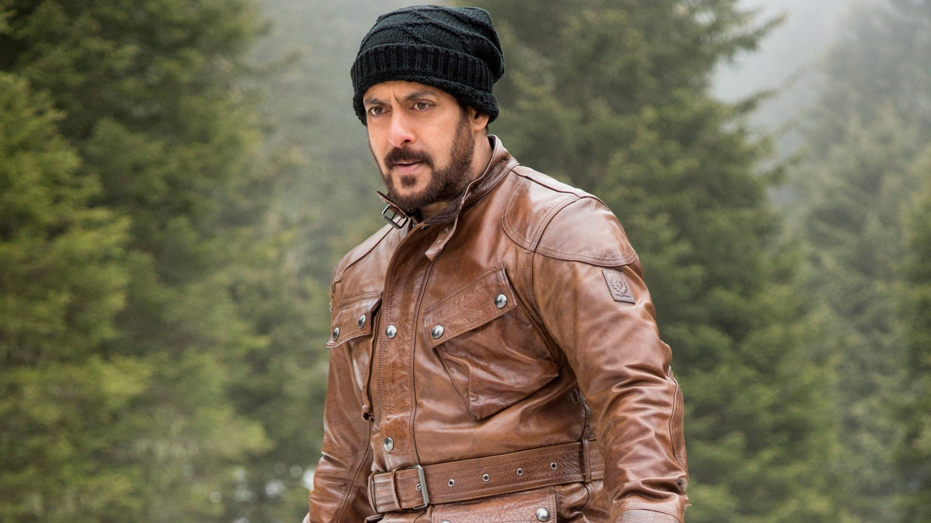 salman khan HD 桌布 壁紙 — 一名身穿棕色皮夾克和黑色毛帽的男子在霧氣瀰漫的森林中警覺地站立，四周綠樹成蔭。