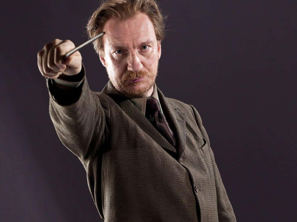 The Hogwarts Professors 桌布 壁紙 — 一名身穿棕色西裝的男子在深色背景下，專注而強烈地向前舉起魔杖。
