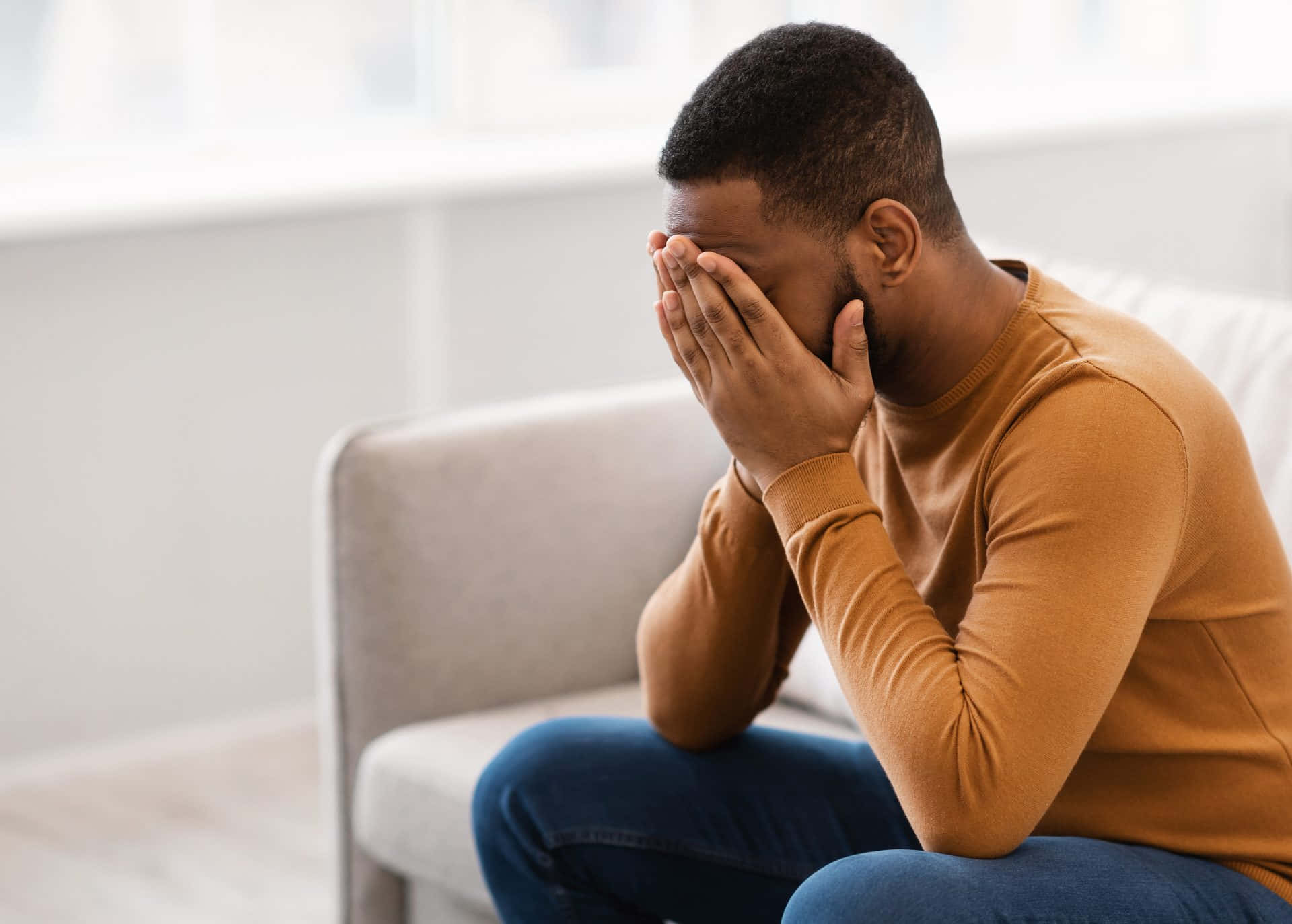 Depressed 桌布 壁紙 — 一名身穿棕褐色毛衣的男子坐在淺灰色沙發上，雙手掩面，顯得痛苦或疲憊。