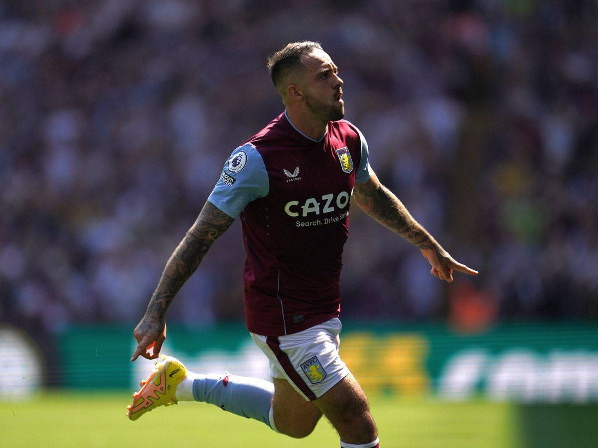 Aston Villa 桌布 壁紙 — 一名身穿棗紅色和淺藍色球衣的足球運動員在陽光明媚的綠色球場上奔跑慶祝，背景是模糊的體育場人群。