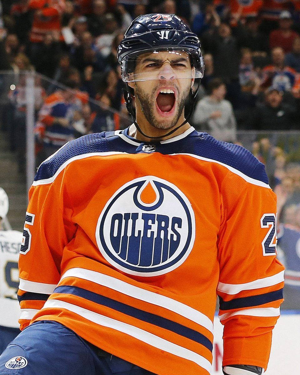 Canadian 桌布 壁紙 — 一名身穿橙色 Oilers 球衣的冰球運動員在比賽中熱情地吶喊，背景有球迷。