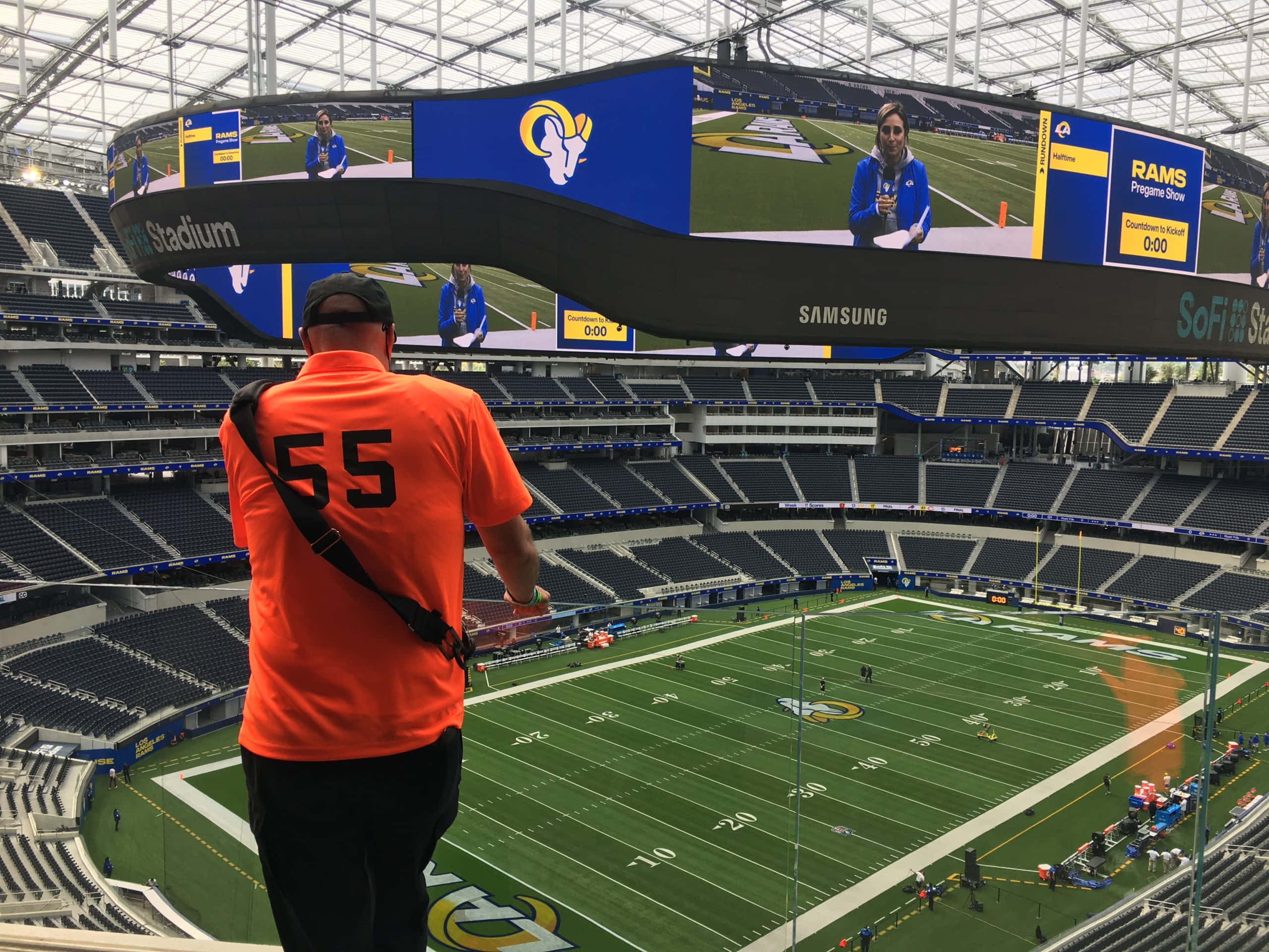 Sofi Stadium 桌布 壁紙 — 一名身穿橙色55號球衣的球迷站在空無一人的SoFi Stadium球場上，觀看賽前表演在巨大的弧形螢幕上播放。