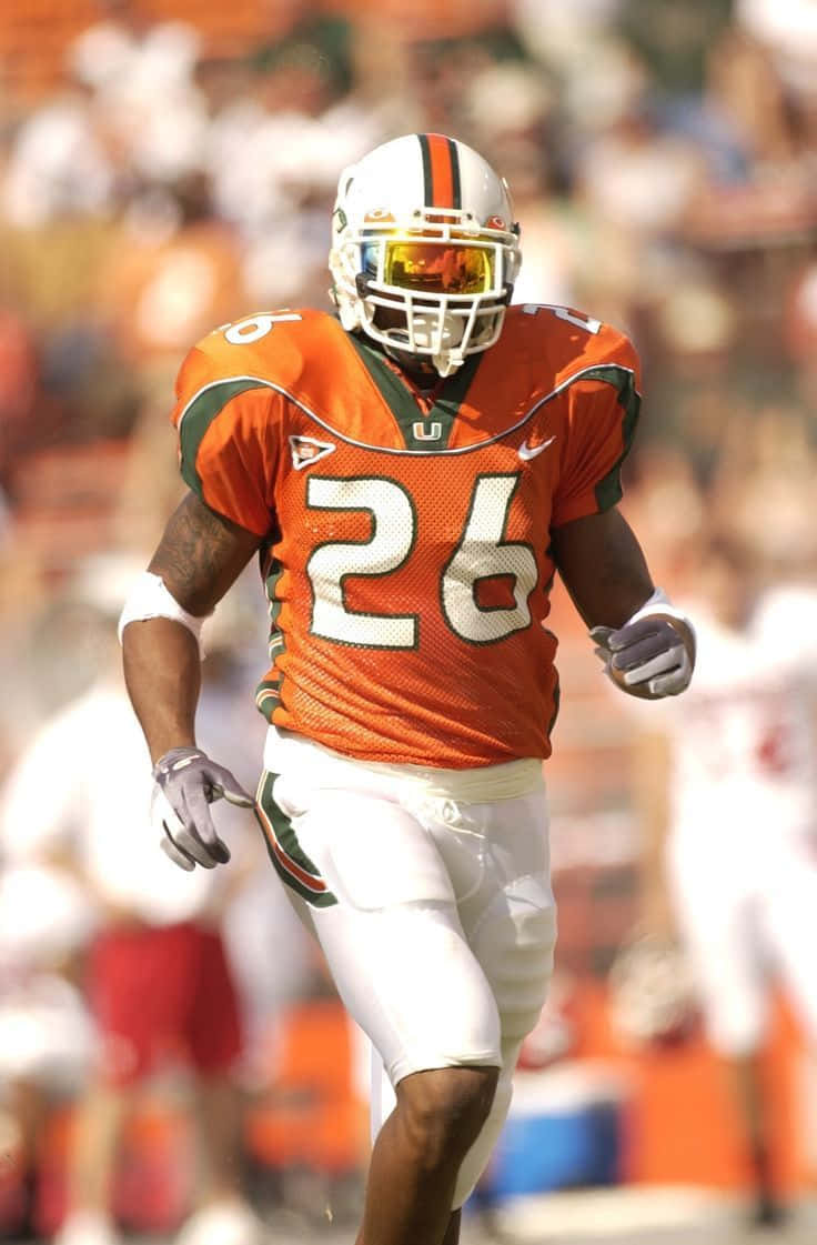 Sean Taylor 桌布 壁紙 — 一名身穿橙色和綠色球衣、號碼26的足球運動員在陽光明媚的球場上衝刺，背景是模糊的體育場人群。
