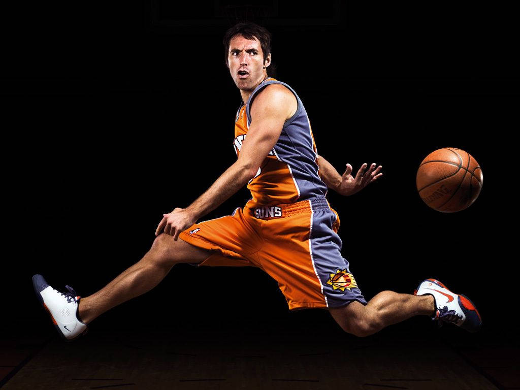 NBA 桌布 壁紙 — 一名身穿橙色和藍色太陽隊球衣的籃球運動員在純黑色背景下低身運球。