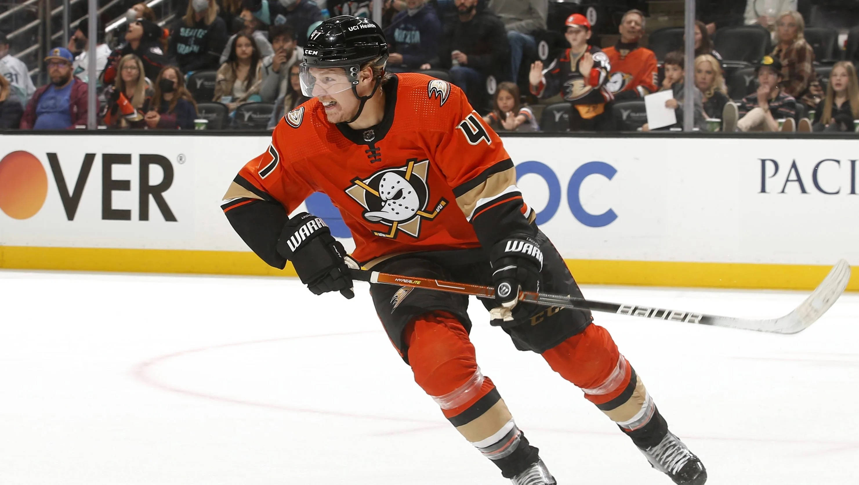 hockey 桌布 壁紙 — 一名身穿橙色和黑色球衣的冰球運動員在冰上激烈滑行，背景有觀眾。