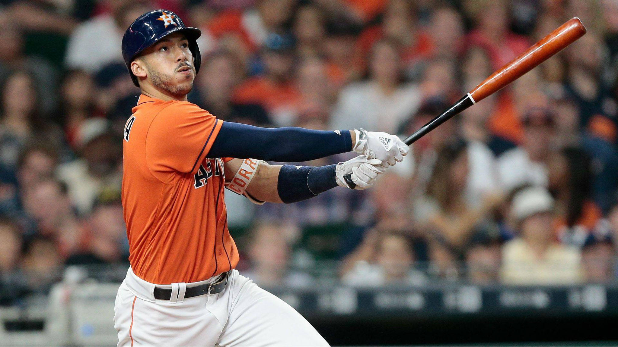 Carlos Correa 桌布 壁紙 — 一名身穿橙色球衣的棒球選手在球場燈光下的夜間比賽中，全神貫注地揮棒。