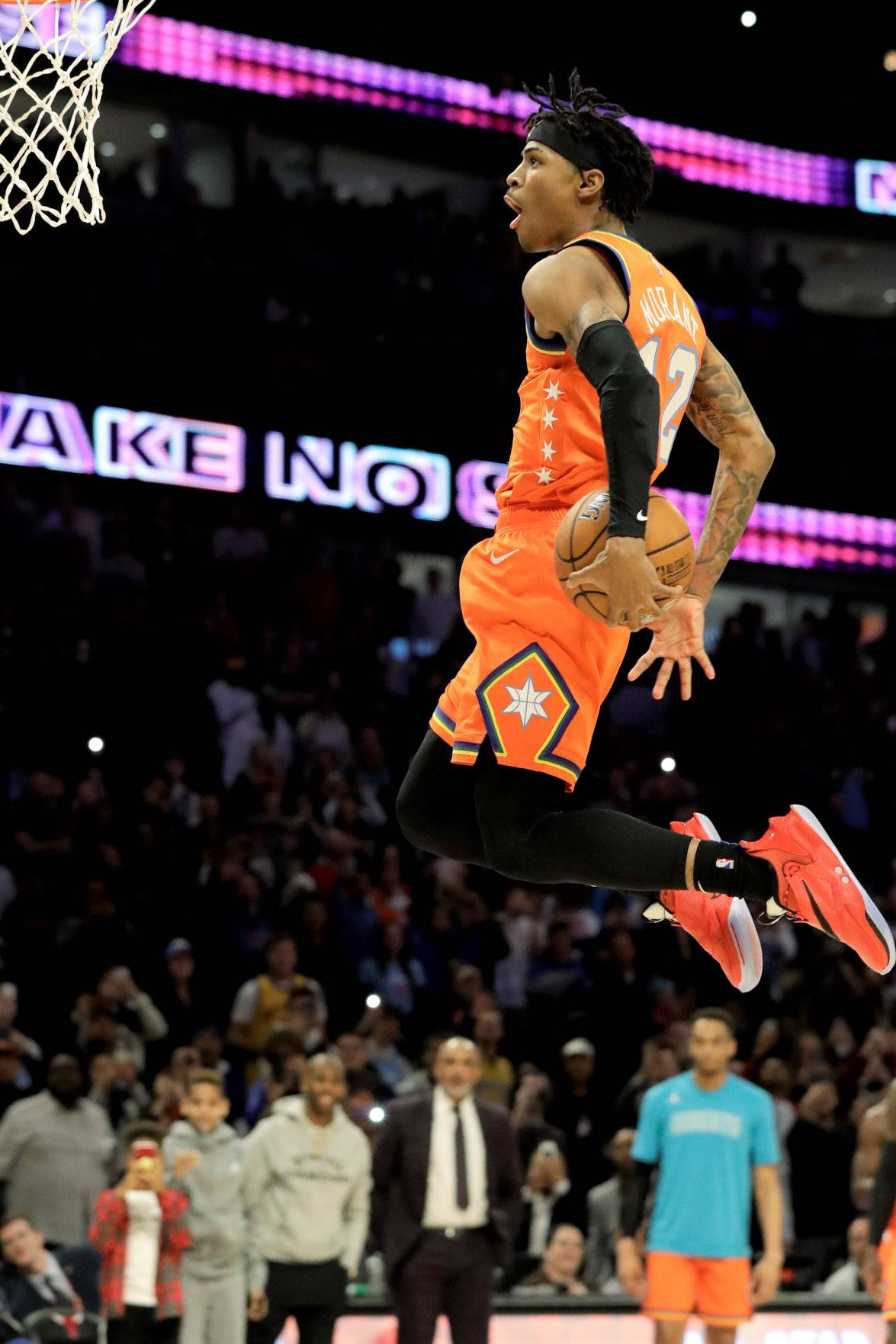 Ja Morant 灌籃 桌布 壁紙 — 一名身穿橙色球衣的籃球運動員在擠滿觀眾的場館中高高躍起，將球灌入上方的籃框。