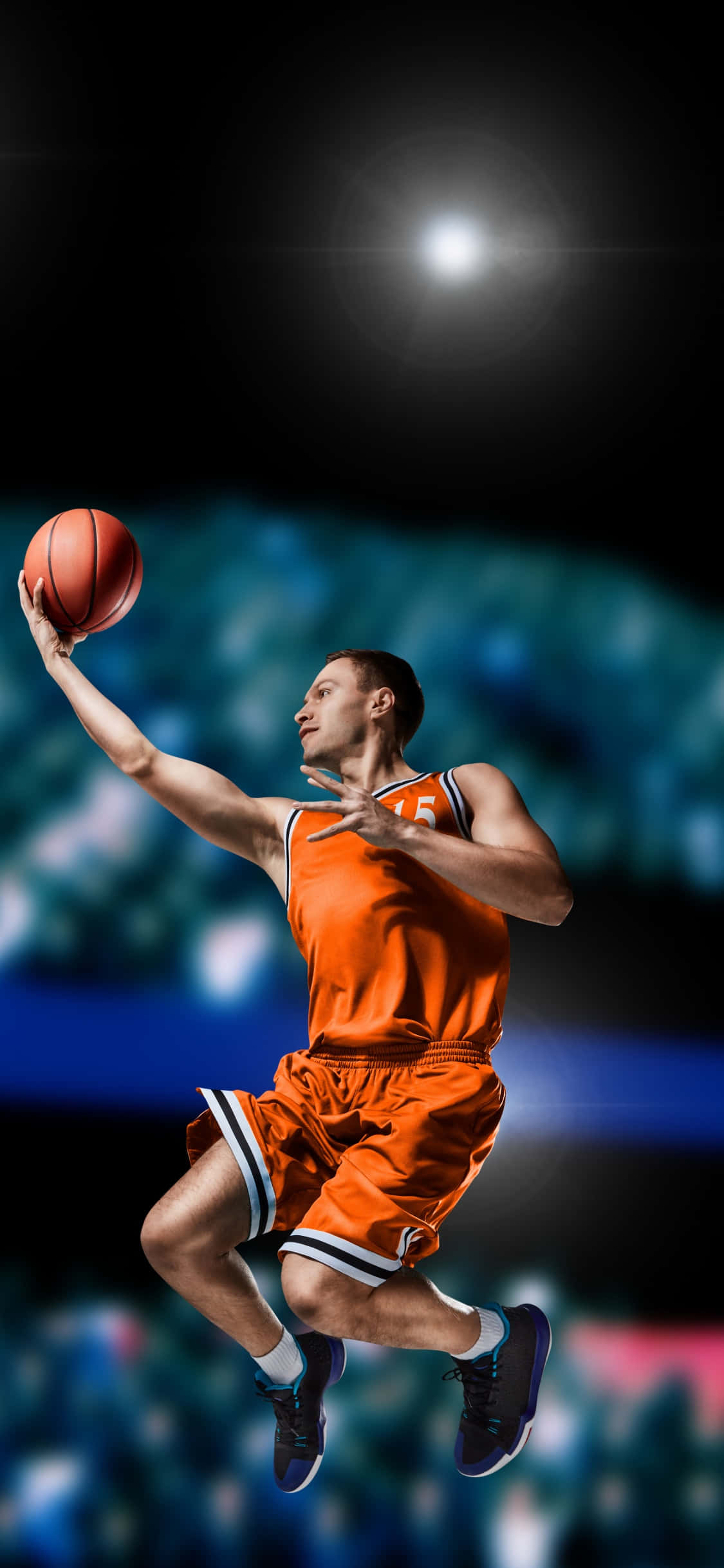 iPhone Xs Basketball 桌布 壁紙 — 一名身穿橙色球衣的籃球運動員在明亮的場館燈光下跳起，手持籃球。